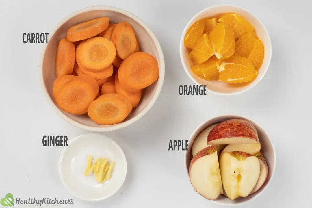Ingredients in separate bowls: sliced carrots, peeled oranges, quartered red apples, julienned ginger knob, 