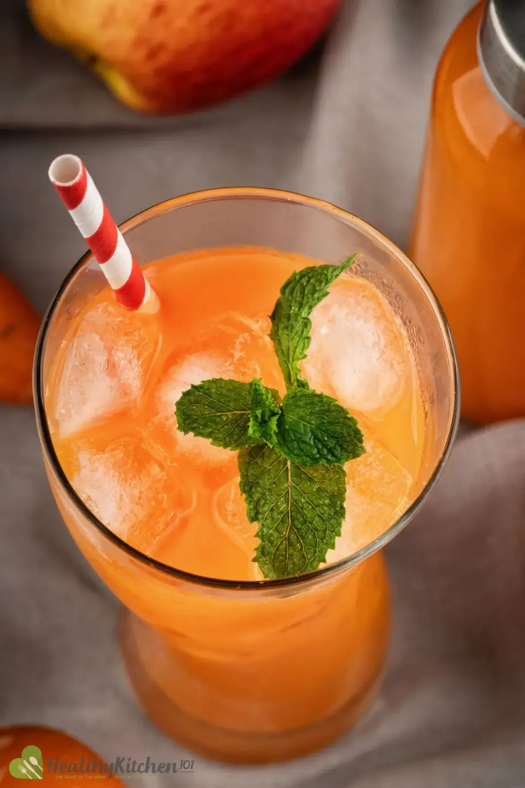 An iced glass of carrot juice with a red striped straw and a mint sprig