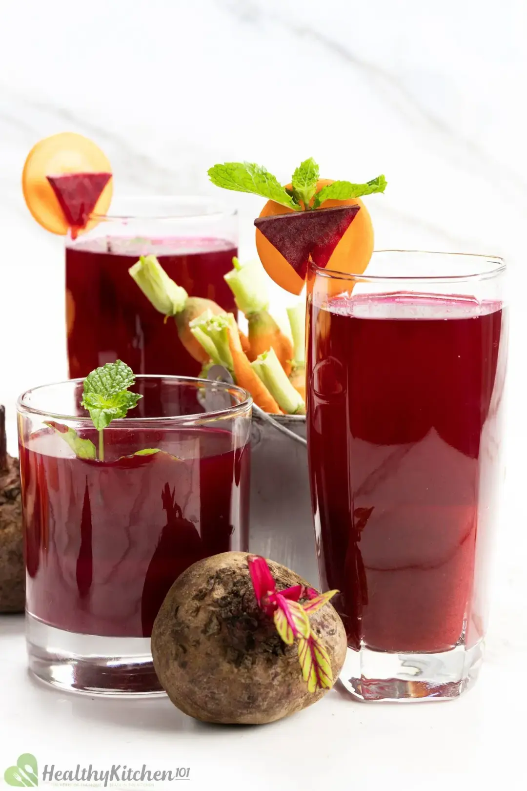 Three glasses of beet juice with carrot as garnish and a beetroot in the front