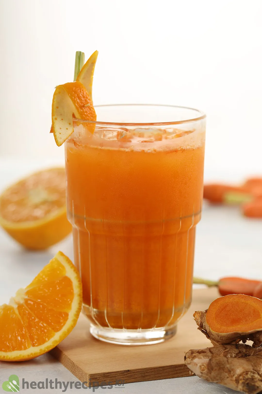 a glass of carrot turmeric juice on a wooden tray decorated with orange wedge and turmeric root