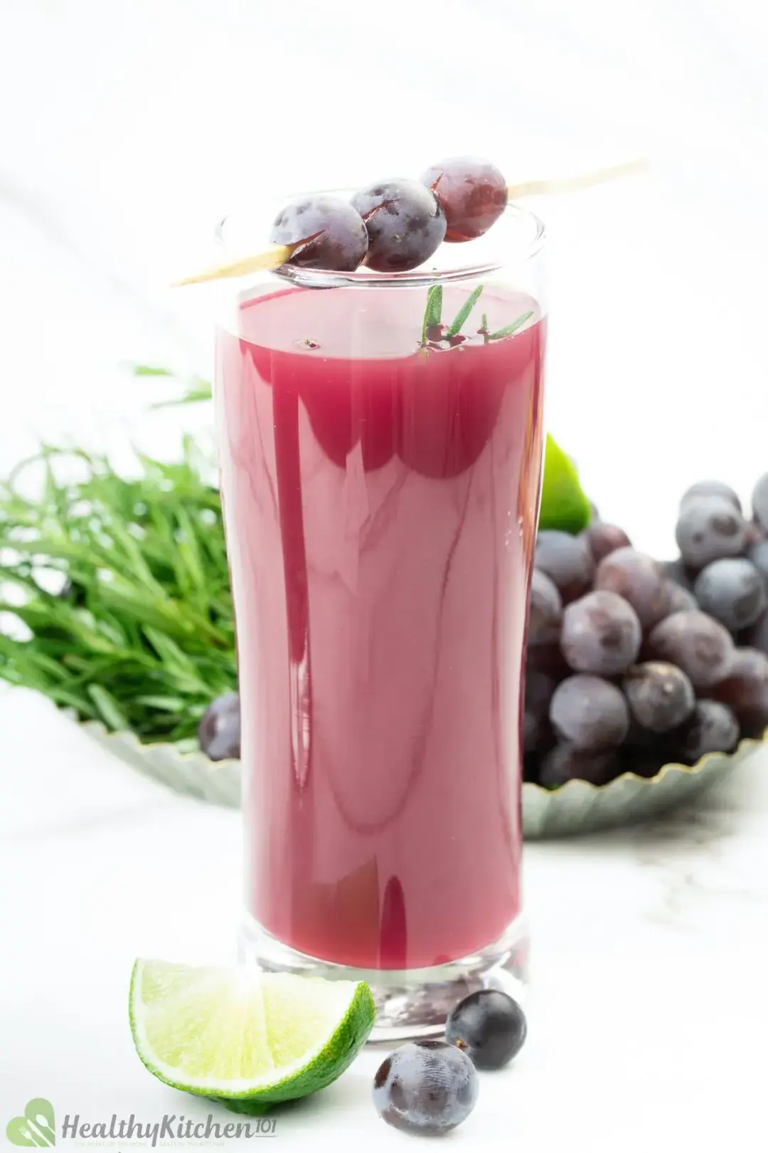 A glass of grape juice with grapes, lime wedge, and a bundle of rosemary