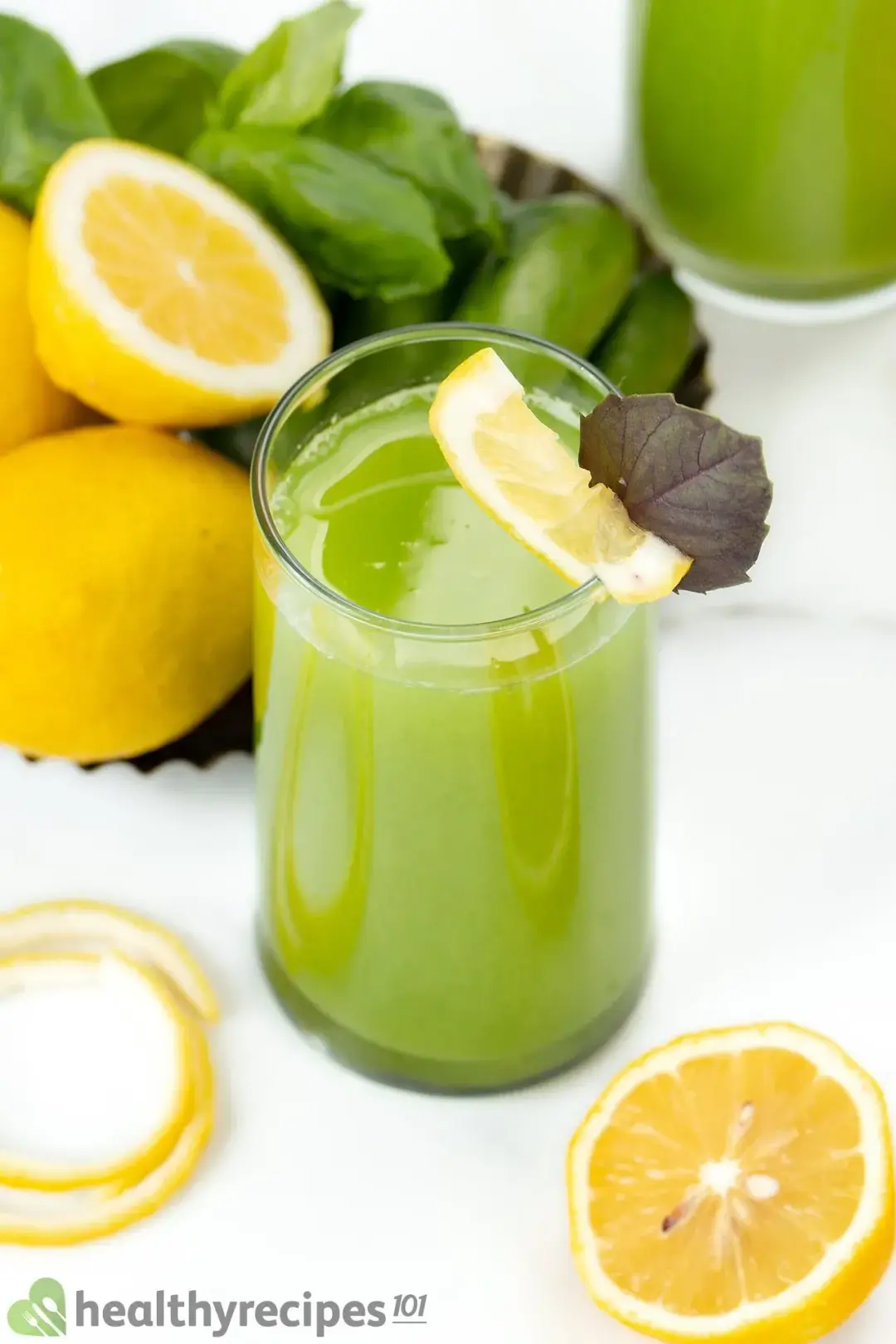 A tall glass of cucumber drink garnished with lemon wheels, whole lemons, and lots of mints