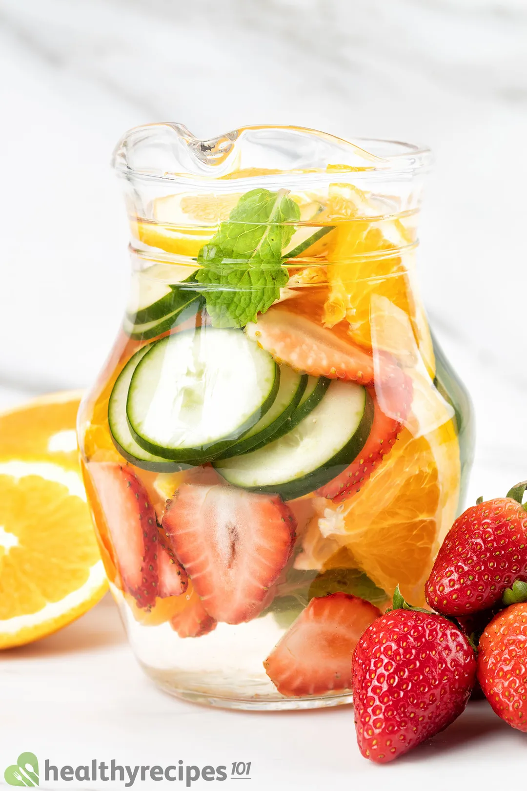 a glass of cucumber water with sliced cucumber, orange and half strawberries