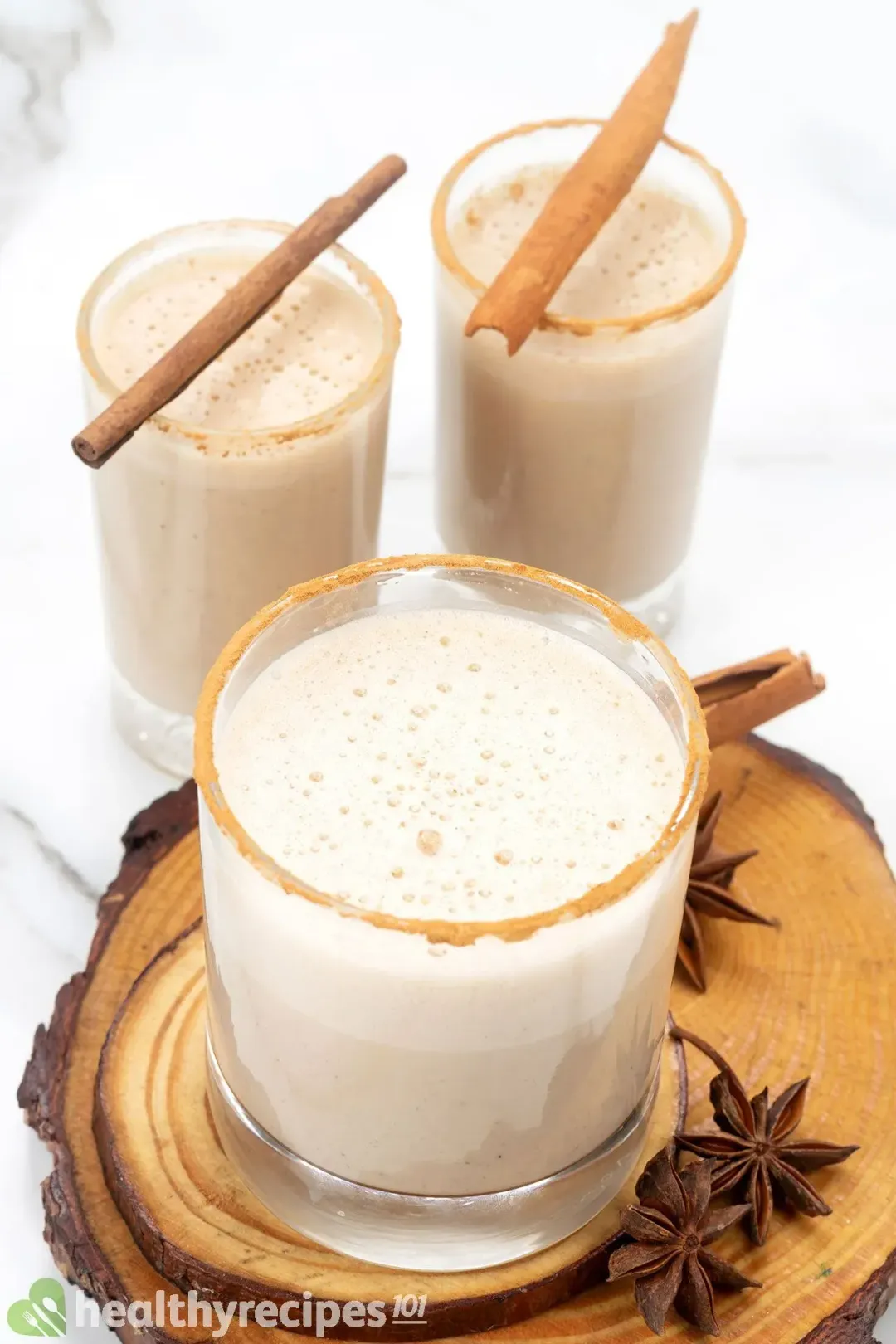 Three glasses of eggnog with cinnamon sticks on top