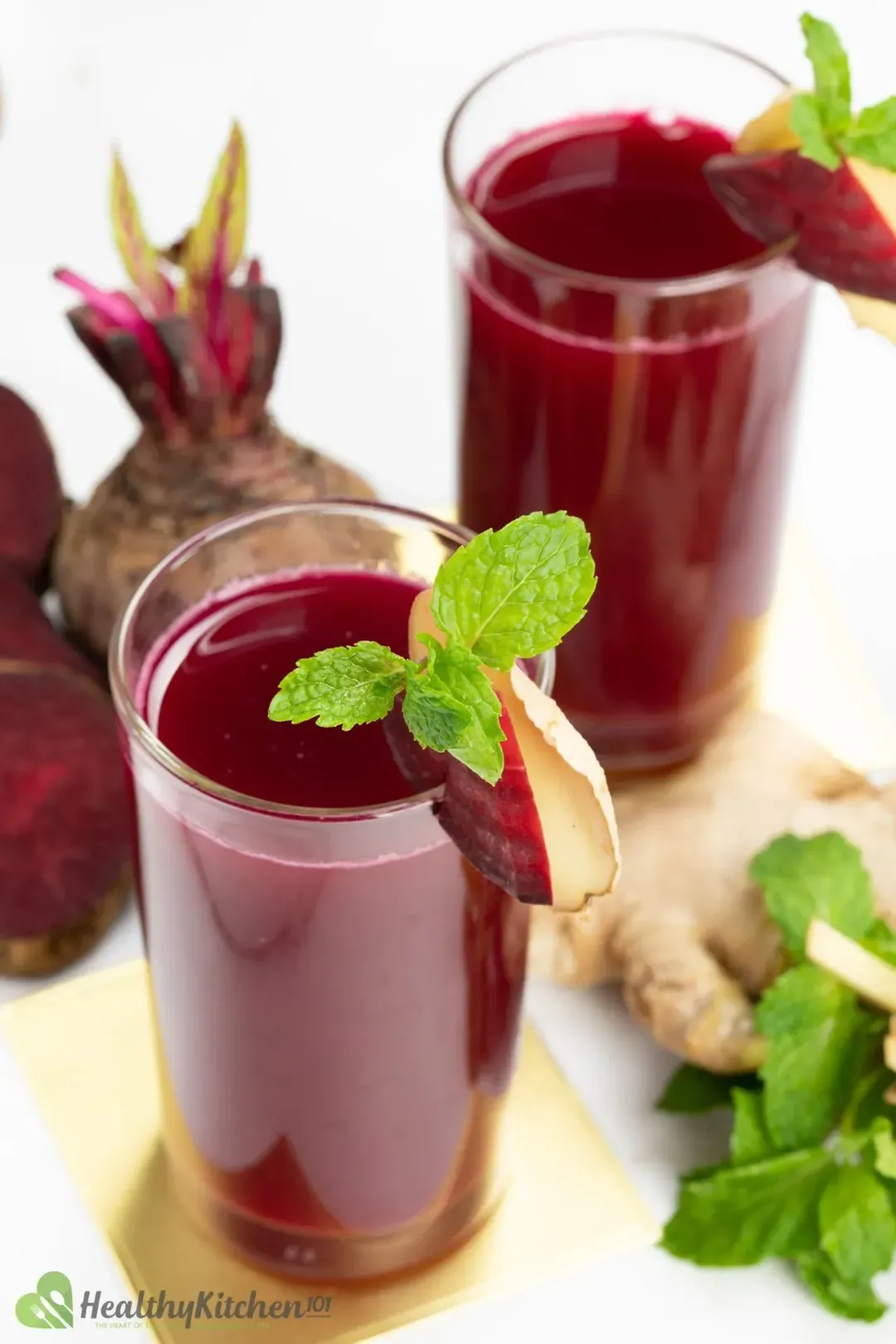 Two glasses of beetroot juice garnished with ginger slices, mint sprigs, and put next to whole beets