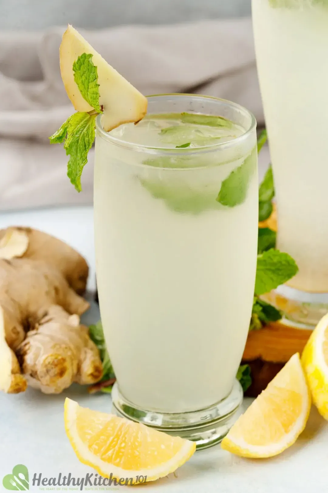 A tall glass of white ginger lemonade garnished with mint leaves, ginger slices, and lemon wedges