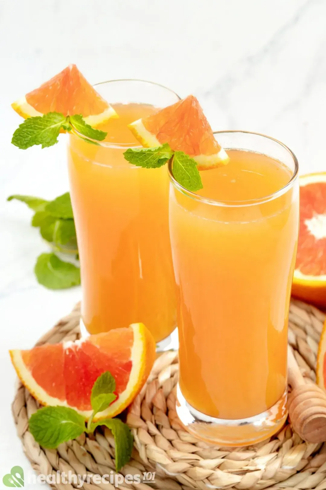 Two glasses of grapefruit juice garnished with mints, grapefruit wedges, and next to a wedge of grapefruit