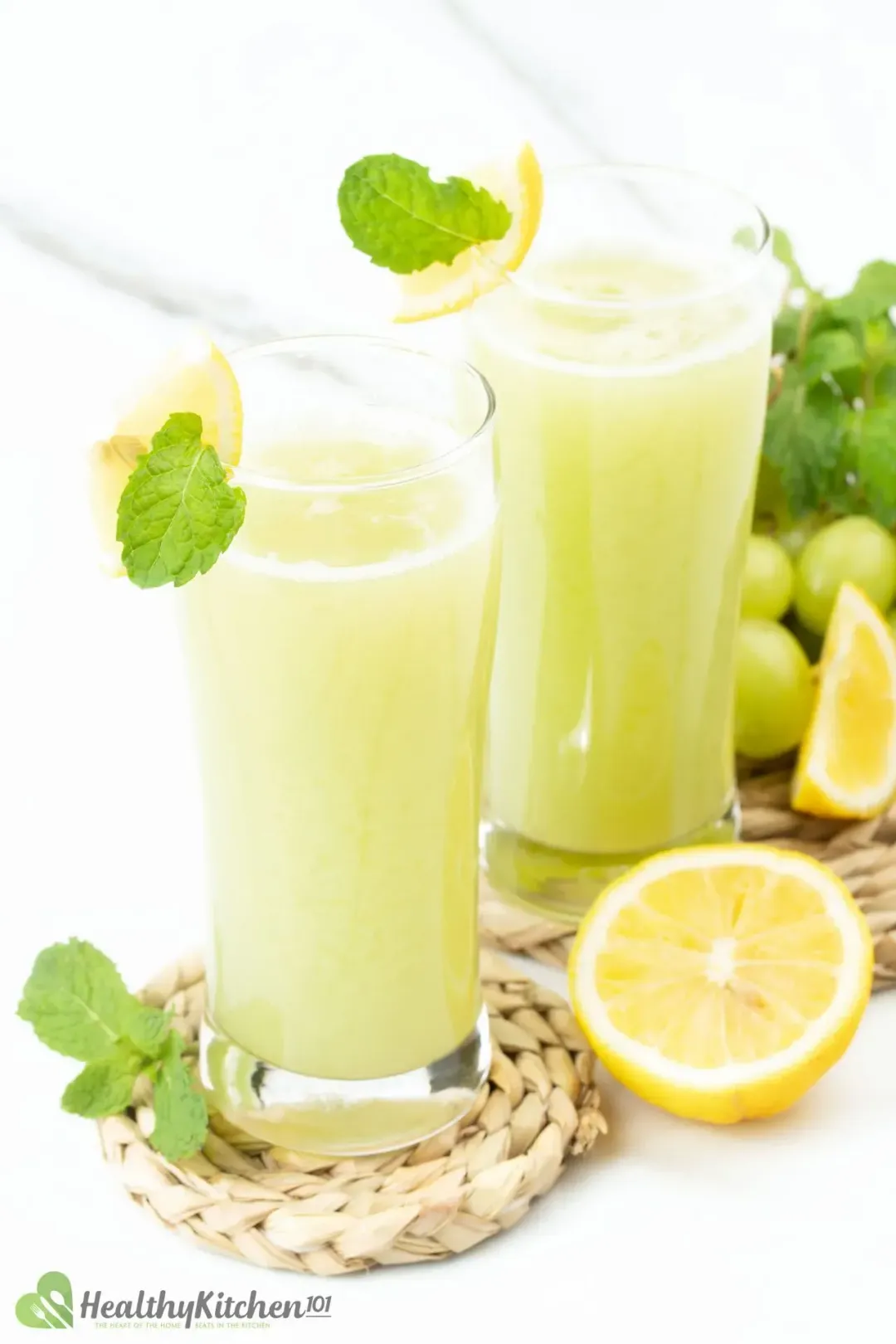 Two glasses of green grape juice with a wedge of lemon and mint leaves placed on their rims