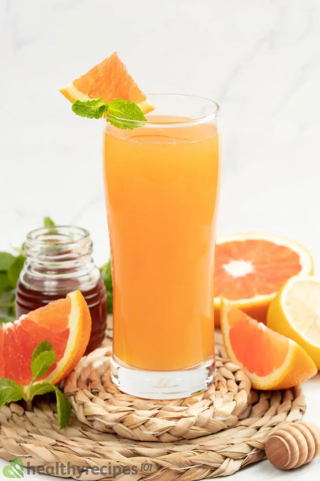 A glass of grapefruit juice garnished with mints, next to grapefruit wedges and a jar of honey