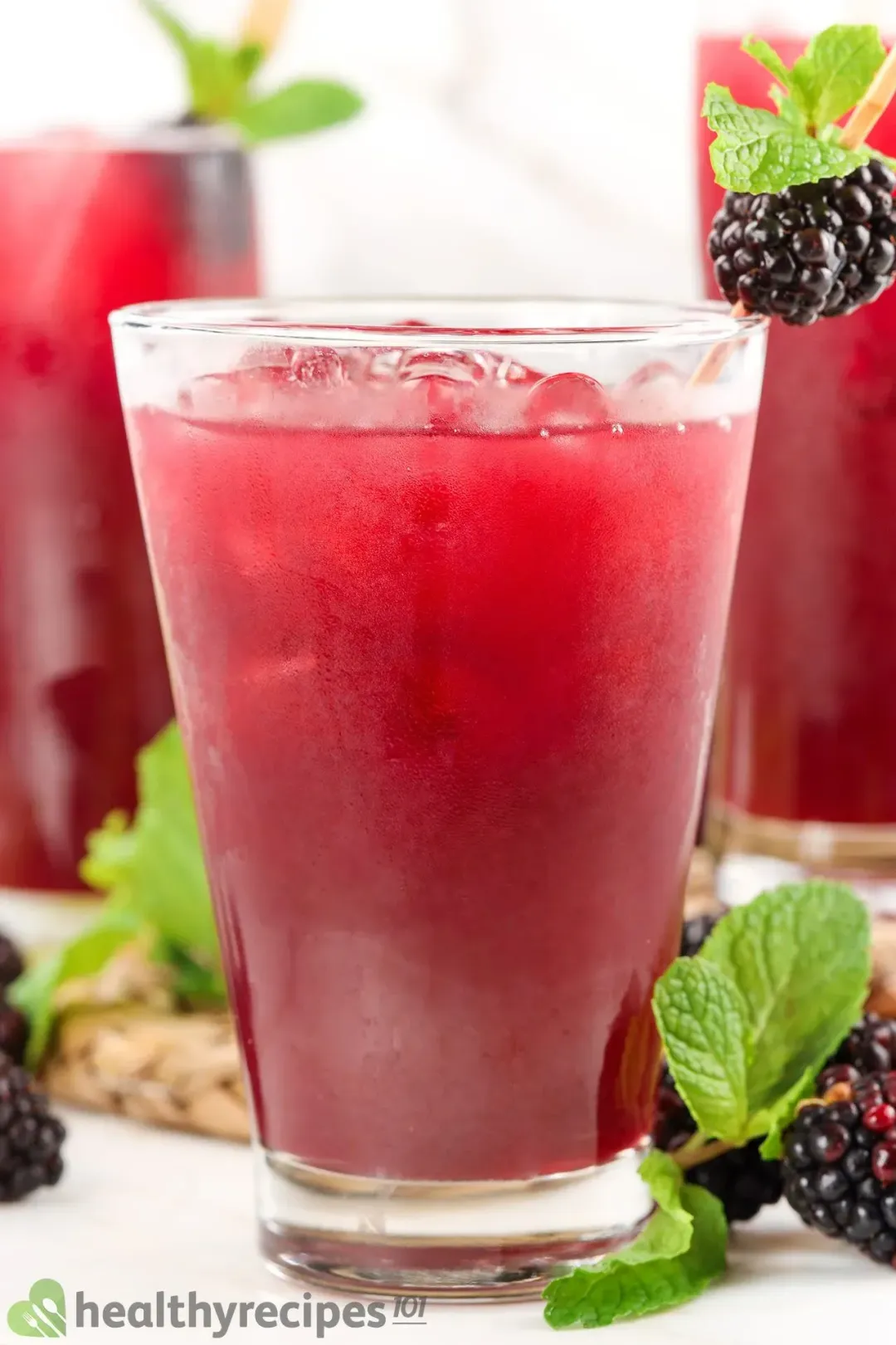 Three iced glasses of pink blackberry juice drinks, garnished with mints and blackberries