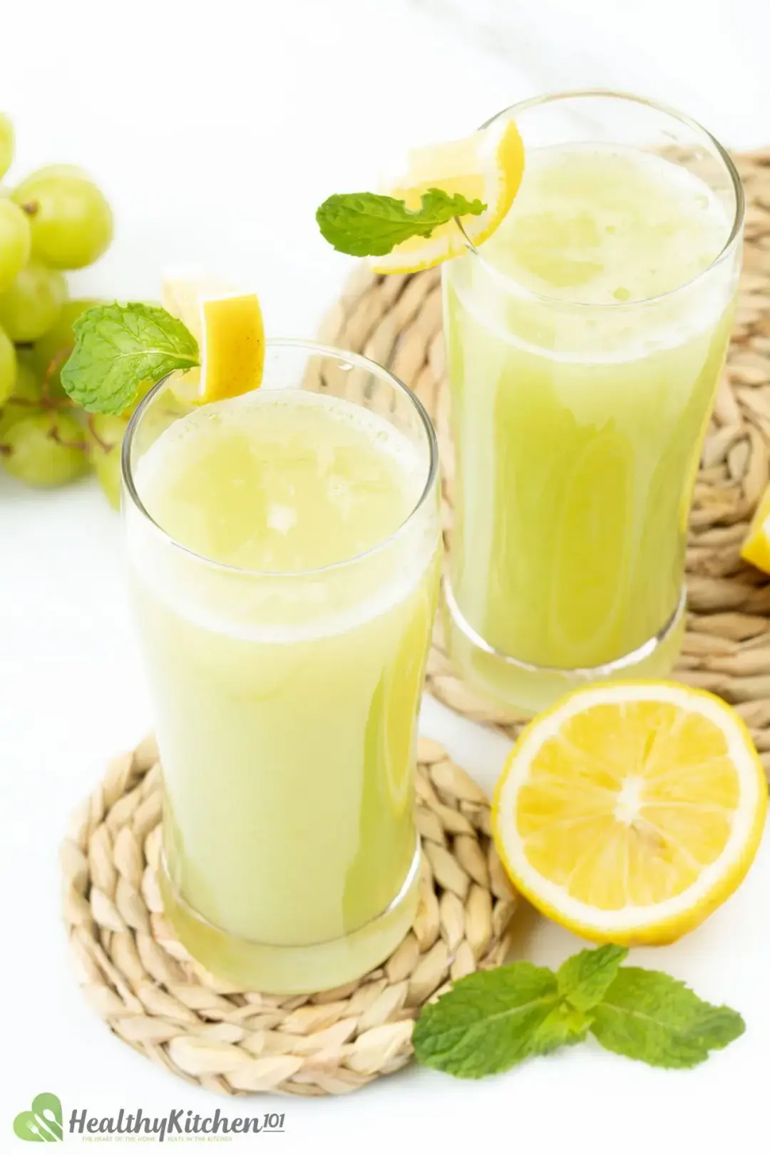 Two glasses of green grape juice placed on two separated rush coasters with lemon and mint leaves on the side for decoration 
