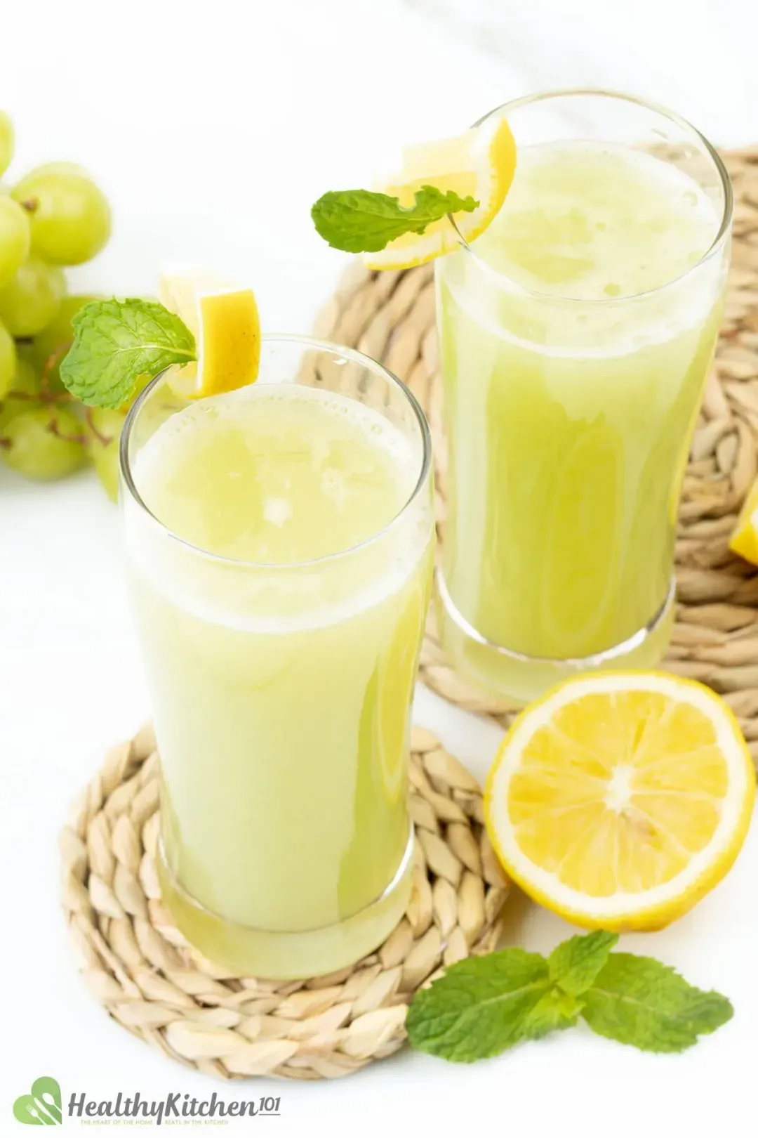 Two glasses of green grape juice placed on two separated rush coasters with lemon and mint leaves on the side for decoration 