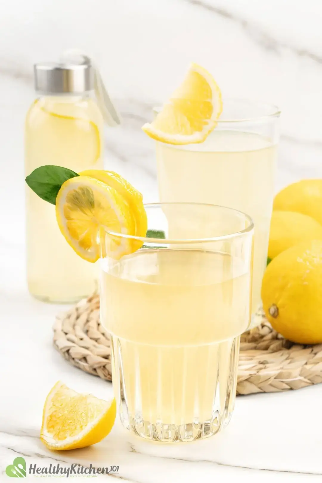 Two glasses of lemonade and lemon wedge garnish, with a bottle of lemonade in the back