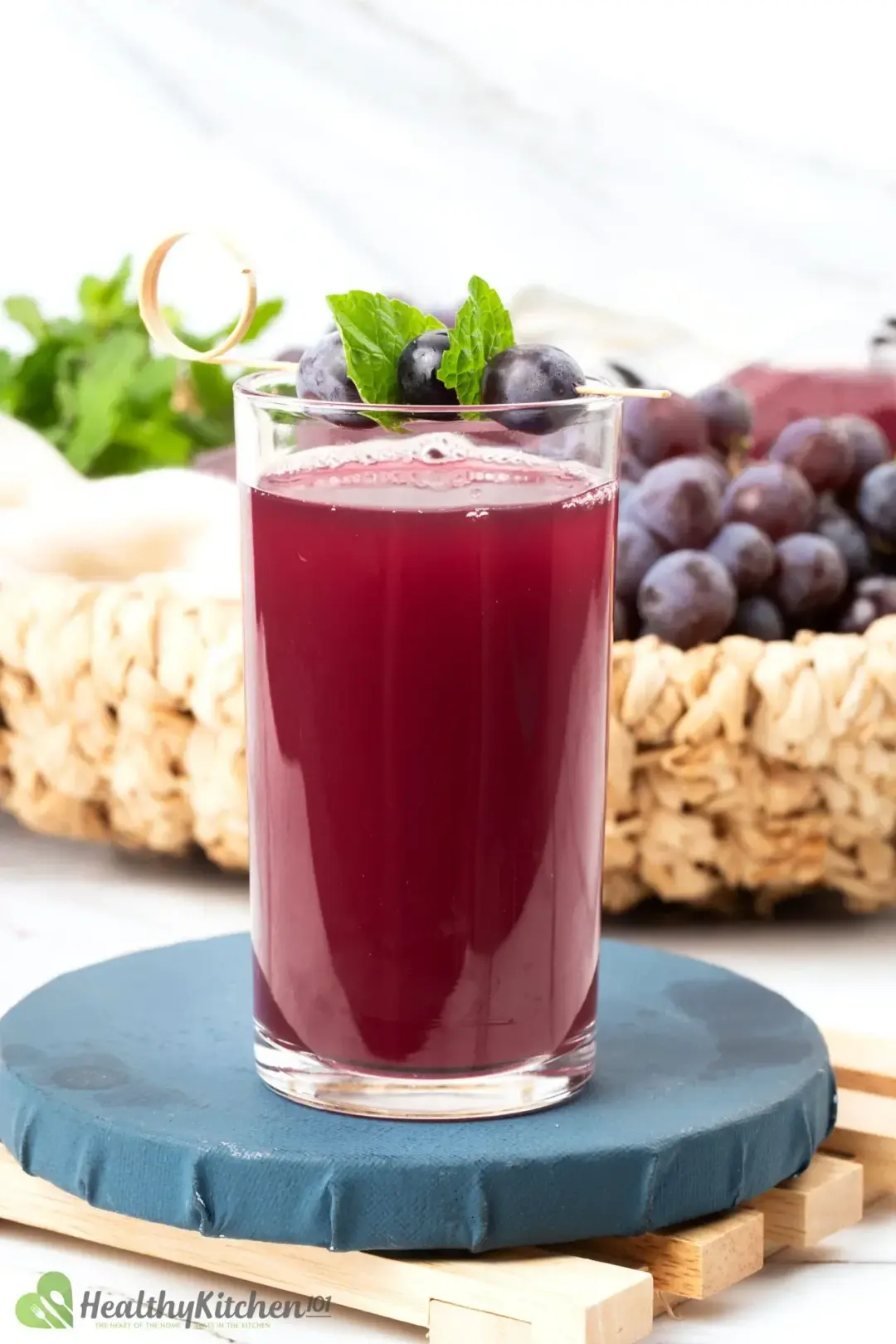 A tall glass of apple cider and grape juice drink garnished with mints and next to a basket of red grapes