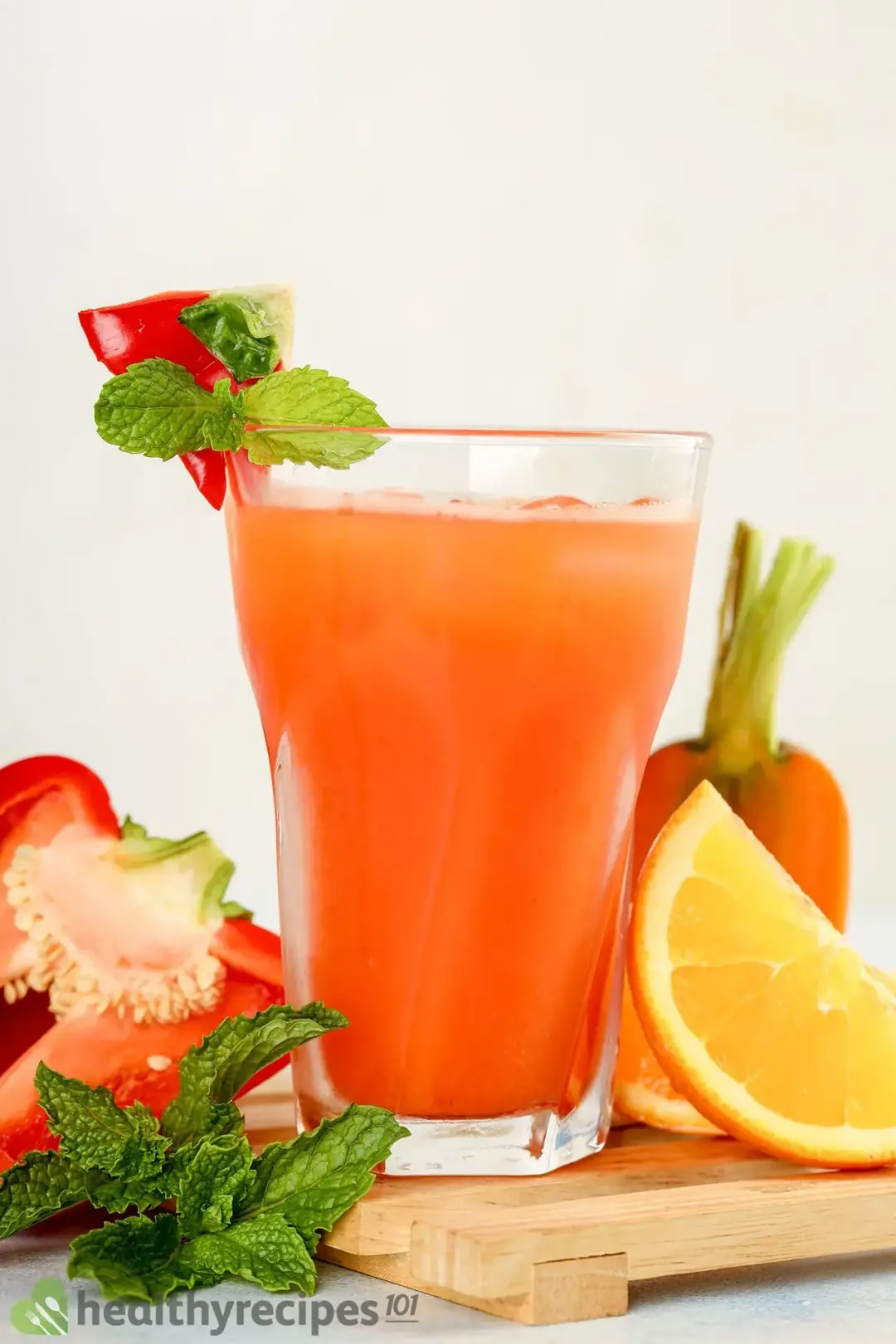 A glass of bell pepper drink garnished with mints, oranges, carrots, and half of a bell pepper