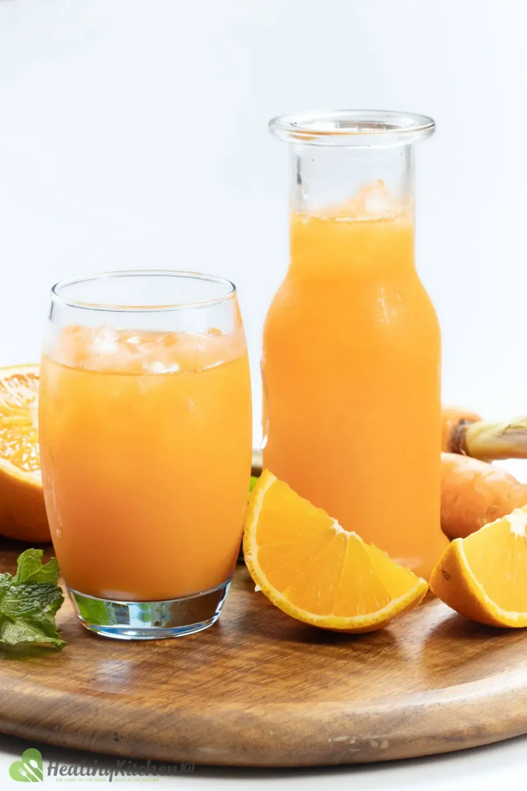 An iced glass and a bottle of orange carrot drinj surrounded by orange wedges