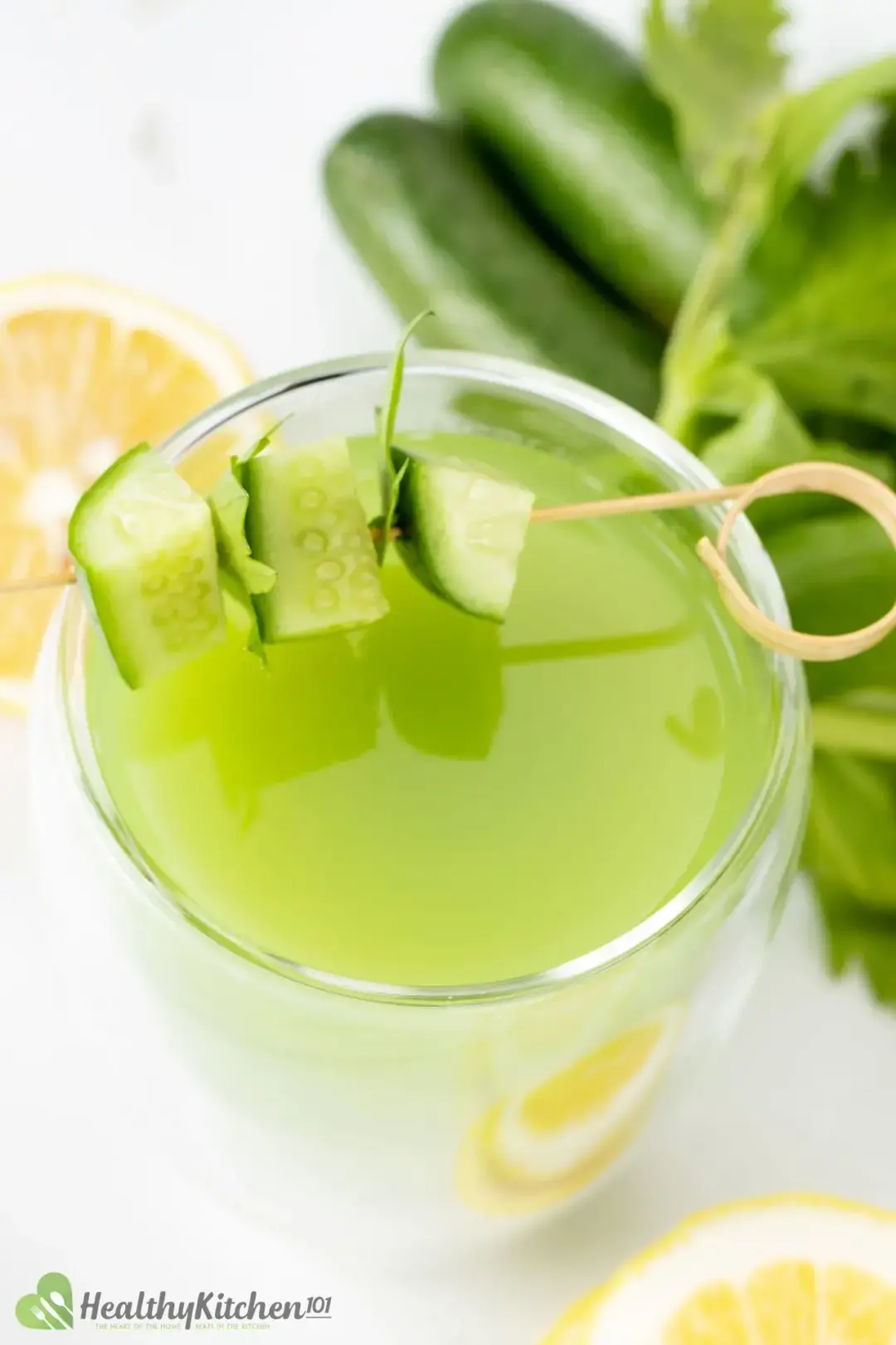 A close-up shot of a cucumber celery drink topped with skewered cucumber and next to whole cucumbers