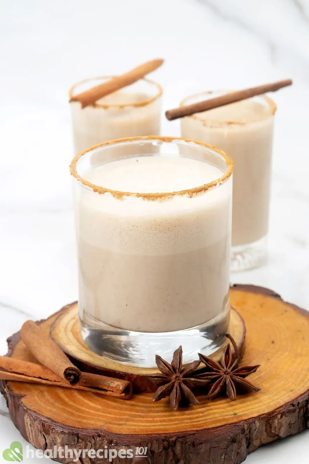 Three classes of foamy eggnog in different sizes topped with cinnamon sticks and surrounded by star anise