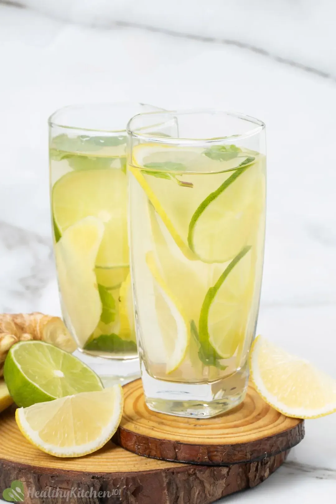 Two glasses of ginger water filled with lemon and lime slices, mints, and put next to extra lemon and limes