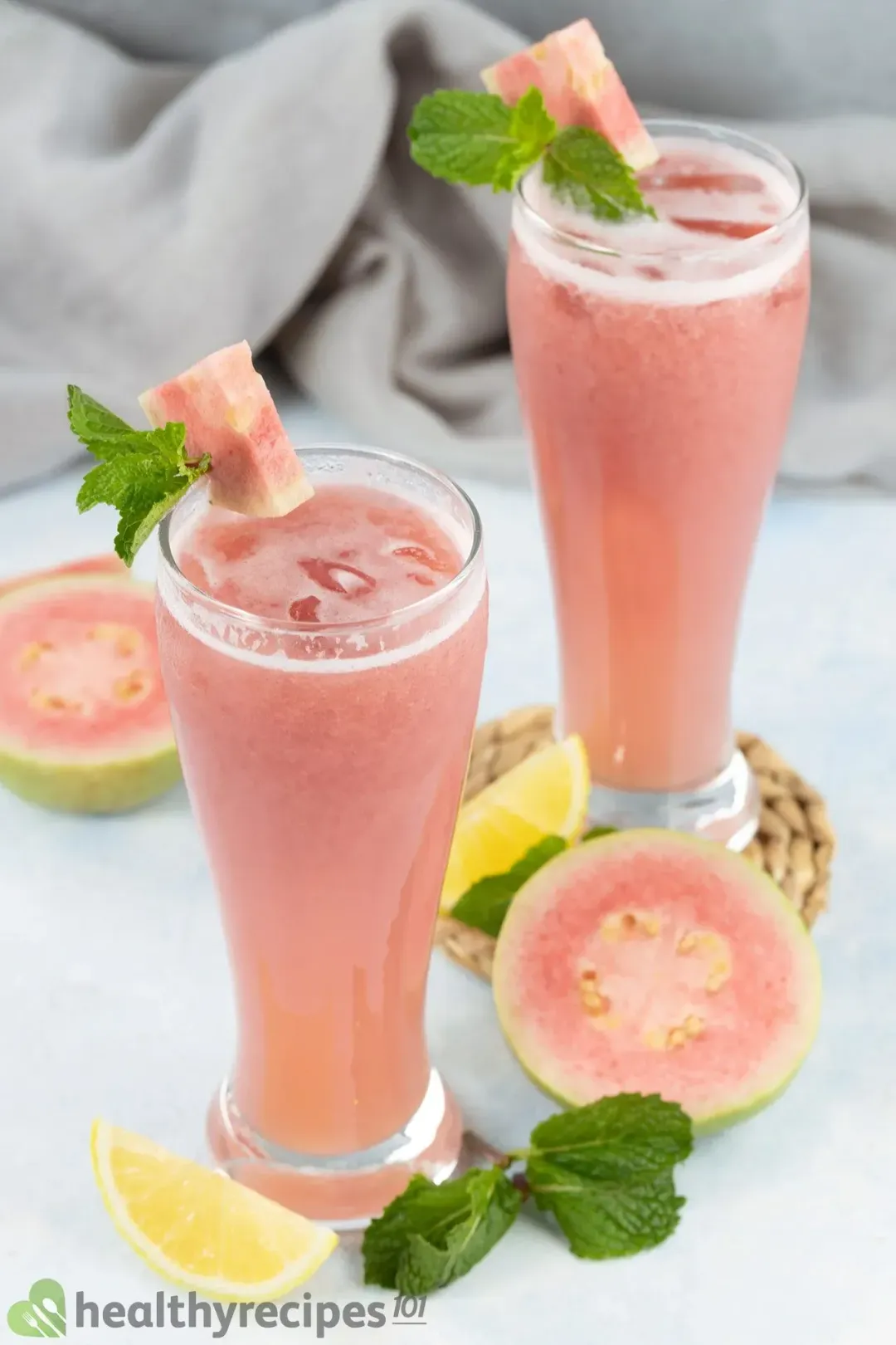 A high-angle shot of two tall guava juice glasses surrounded by lemon wedges and large guava slices