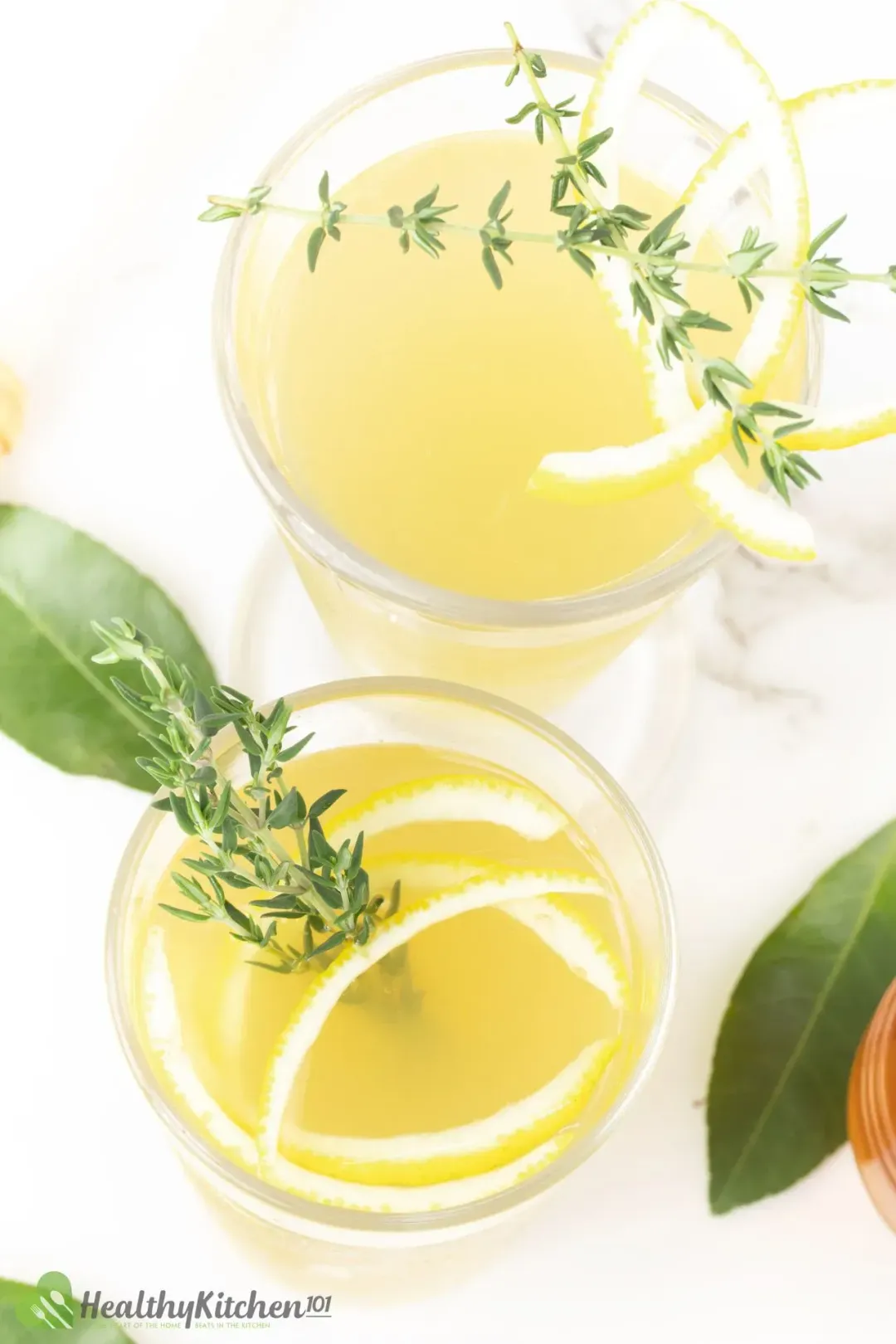 A shot taken from the top of two lemonade glasses garnished with lemon peels, thyme, and lemon leaves