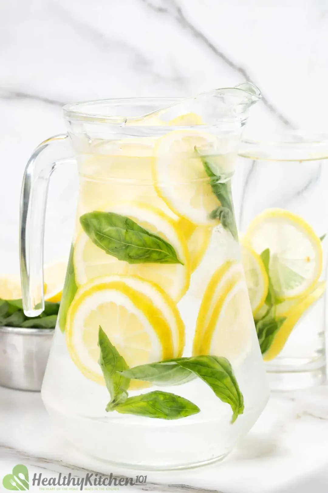 A pitcher of cold water submerging lots of lemon wheels and basil leaves floating about