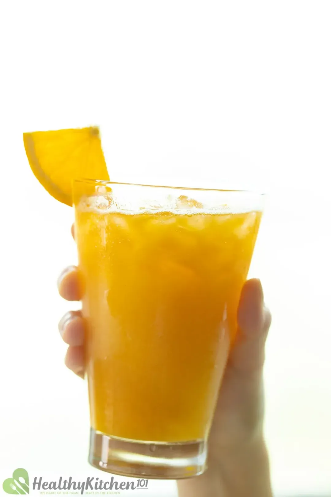 A hand holding an iced glass of orange juice