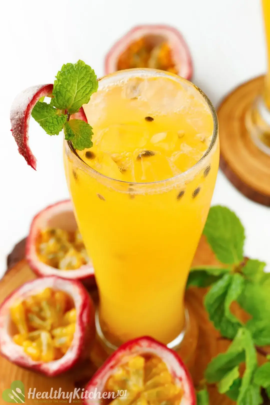 A glass of passion fruit juice with seeds and ice, next to mint leaves and halved passion fruits