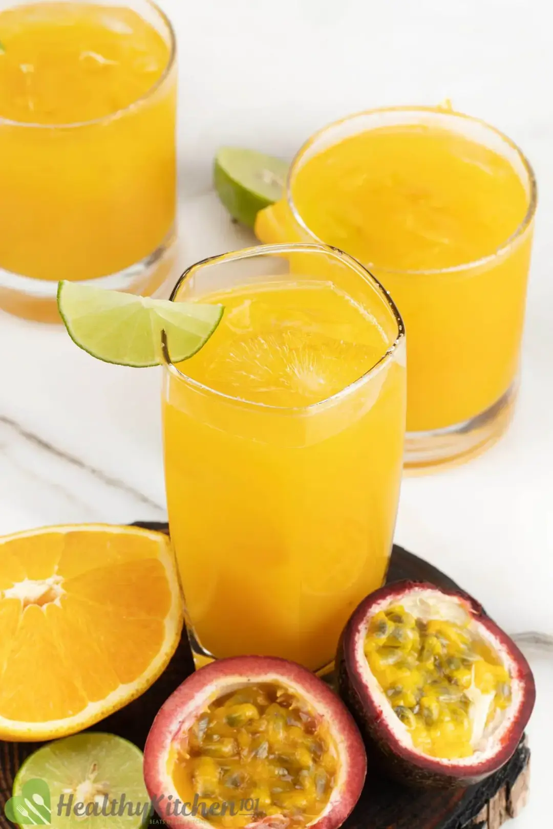 Three glasses of passion fruit margarita with lime wedge, next to passion fruit halves and an orange half
