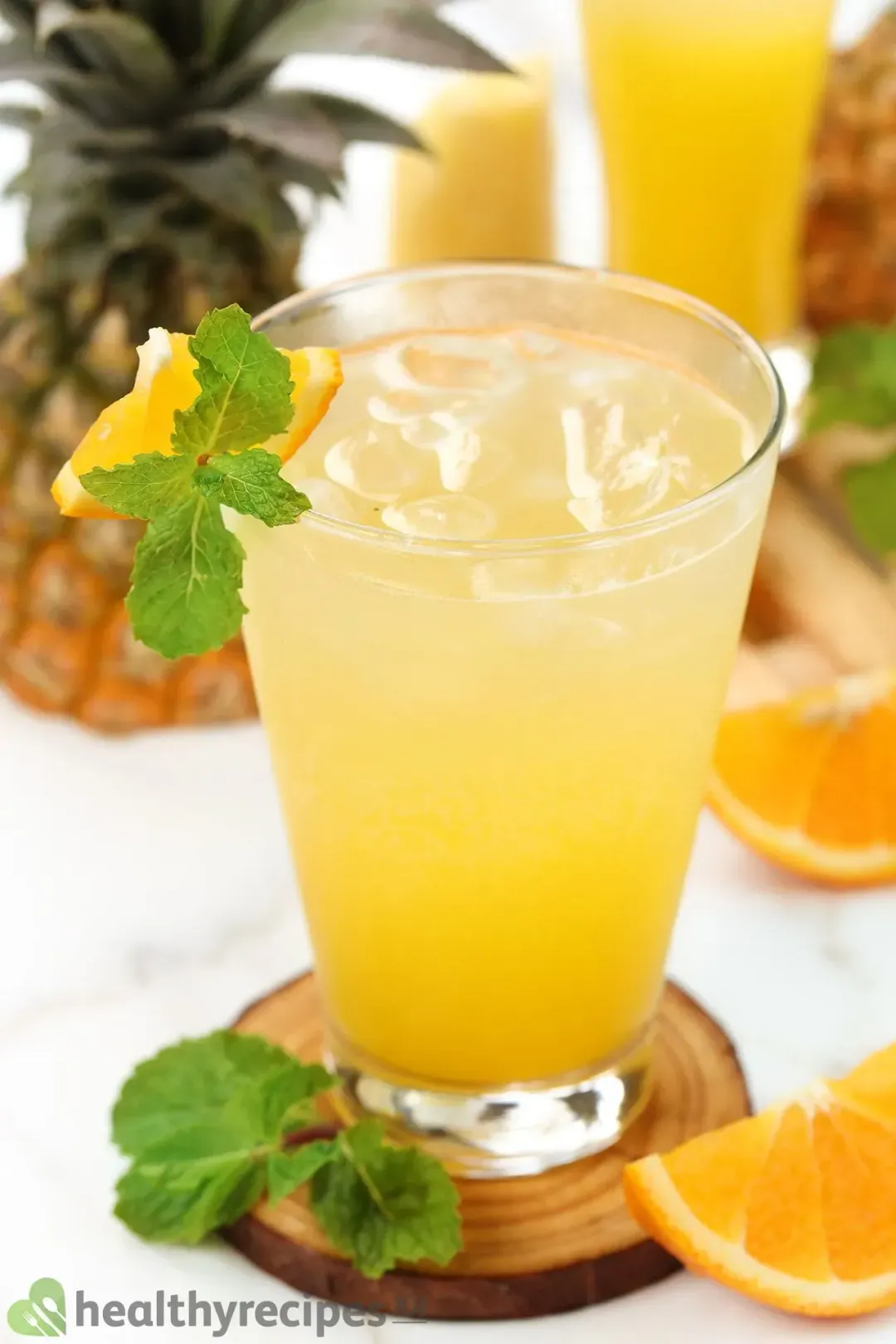 An iced glass of orange juice, rum, and soda put over a wooden coaster and next to mints, orange wedges