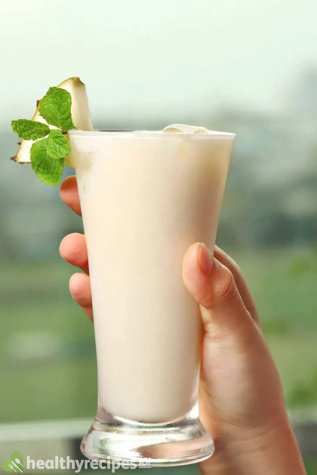 A tall glass of soursop juice with ice, garnished with a wedge of soursop and a mint sprig
