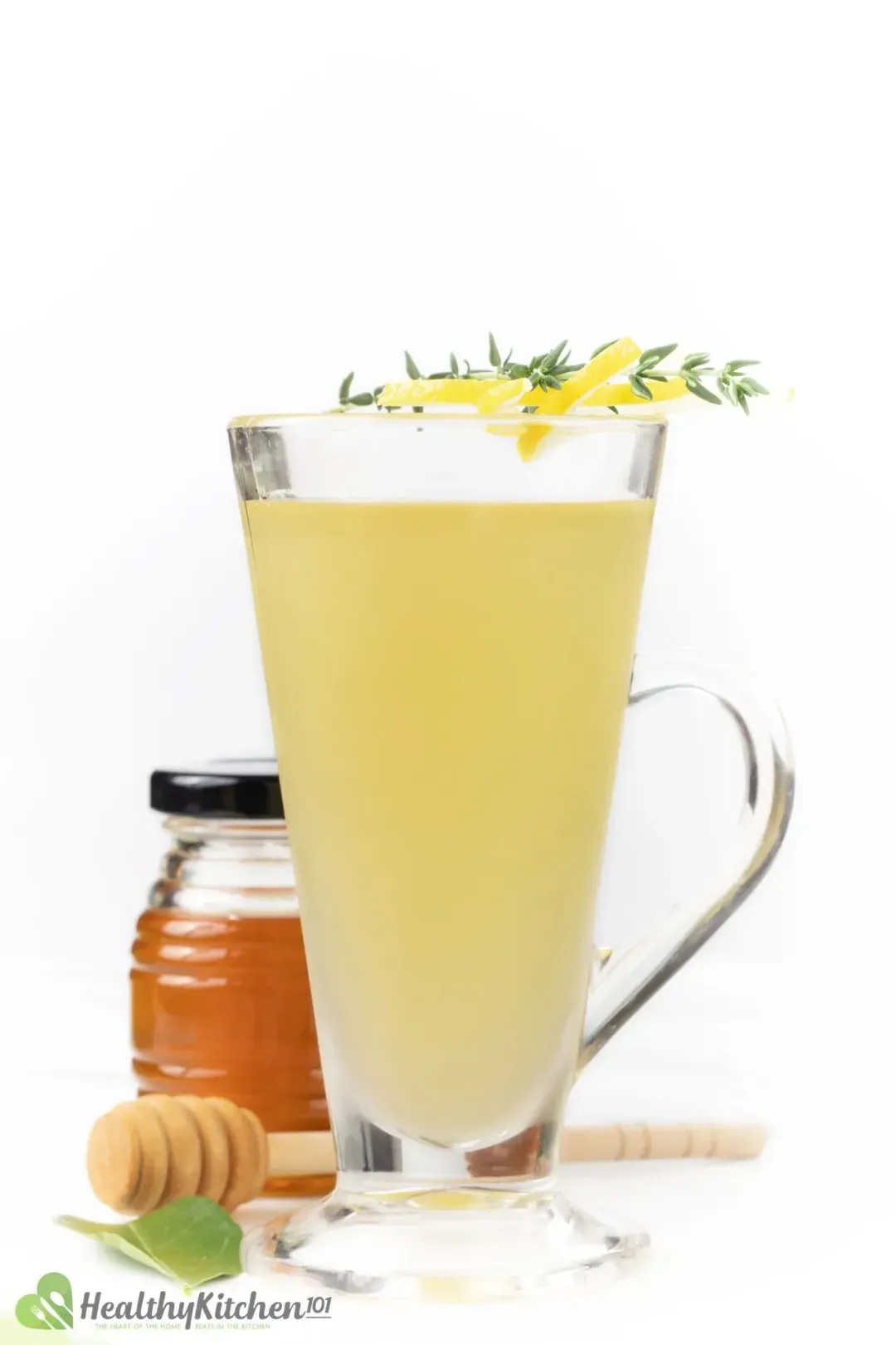 A glass of lemonade topped with thyme, lemon wheels, put in front of a honey jar
