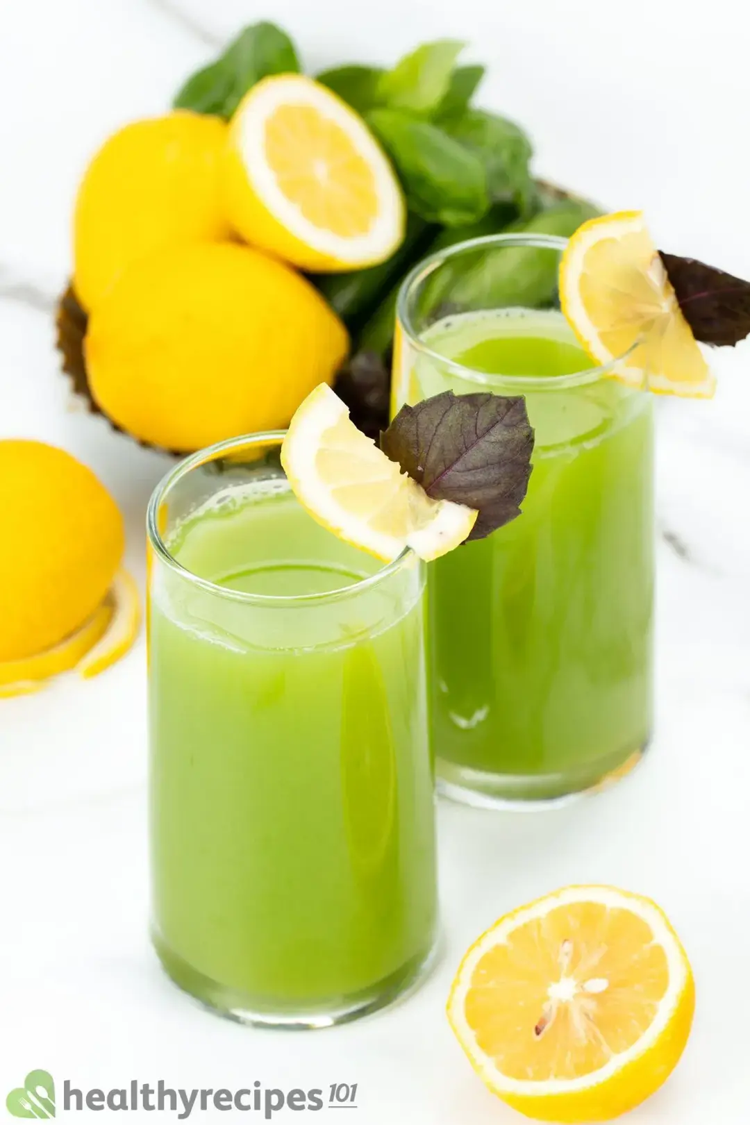 Two glasses of cucumber lemon drinks garnished with lemons, purple leaves, and next to some whole lemons