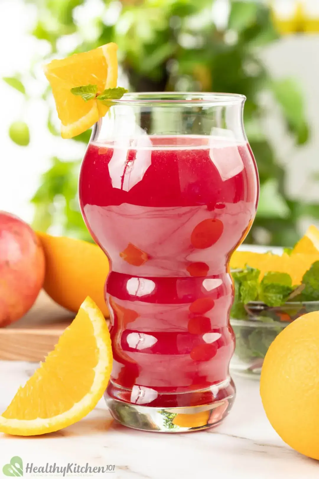 A glass of pomegranate orange juice put next to whole oranges and orange wedges