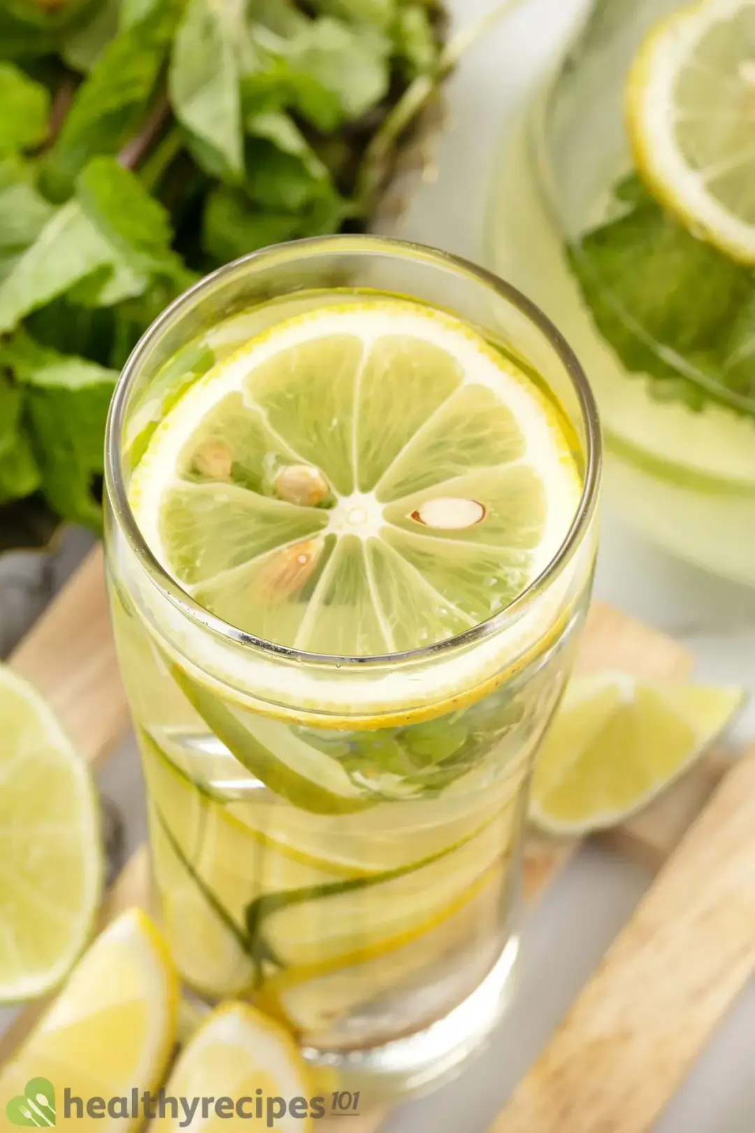 A glass filled with water and lemon wheels, next to lots of mint leaves