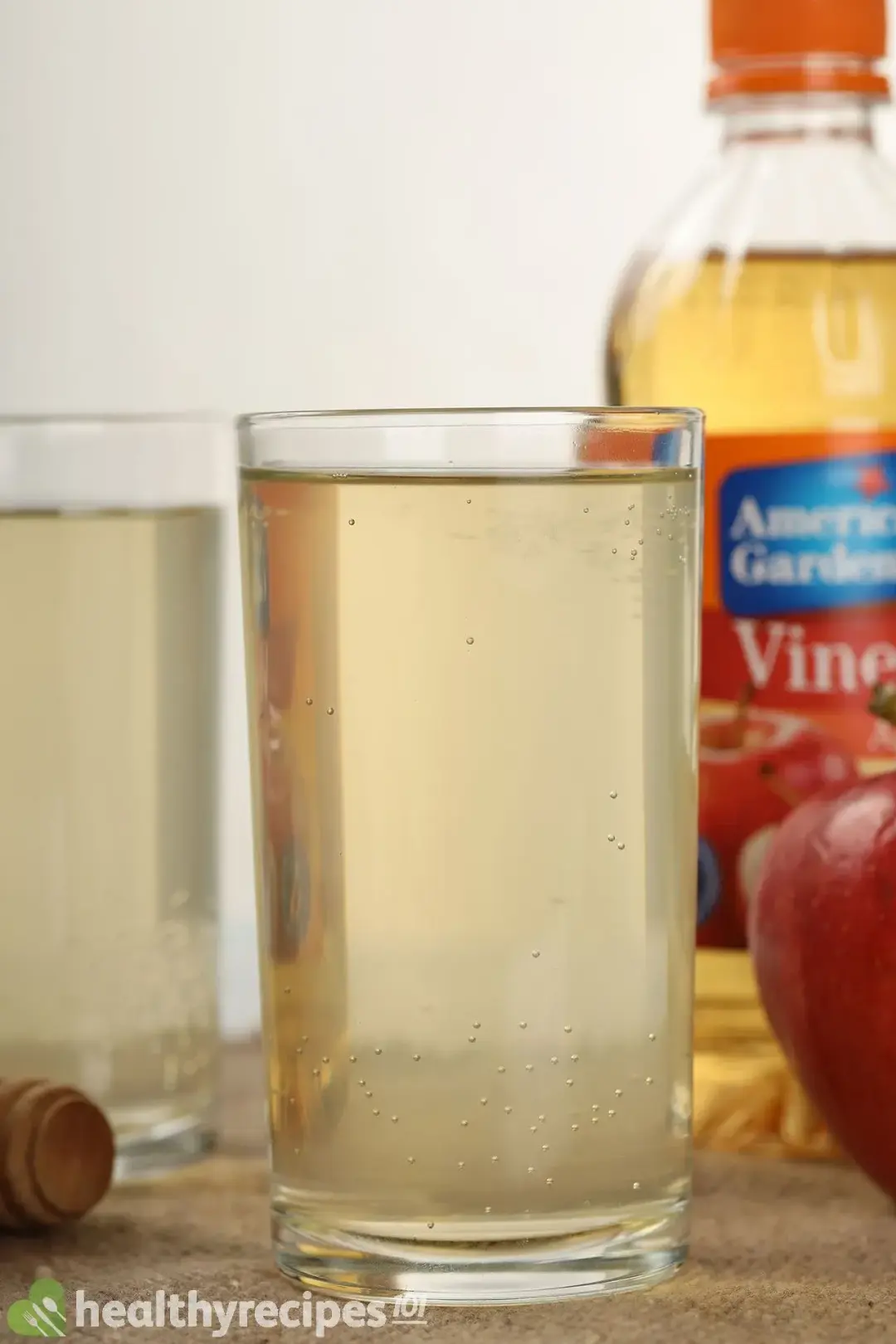 Two tall glasses full of diluted apple cider vinegar and soda, next to a vinegar bottle and an apple