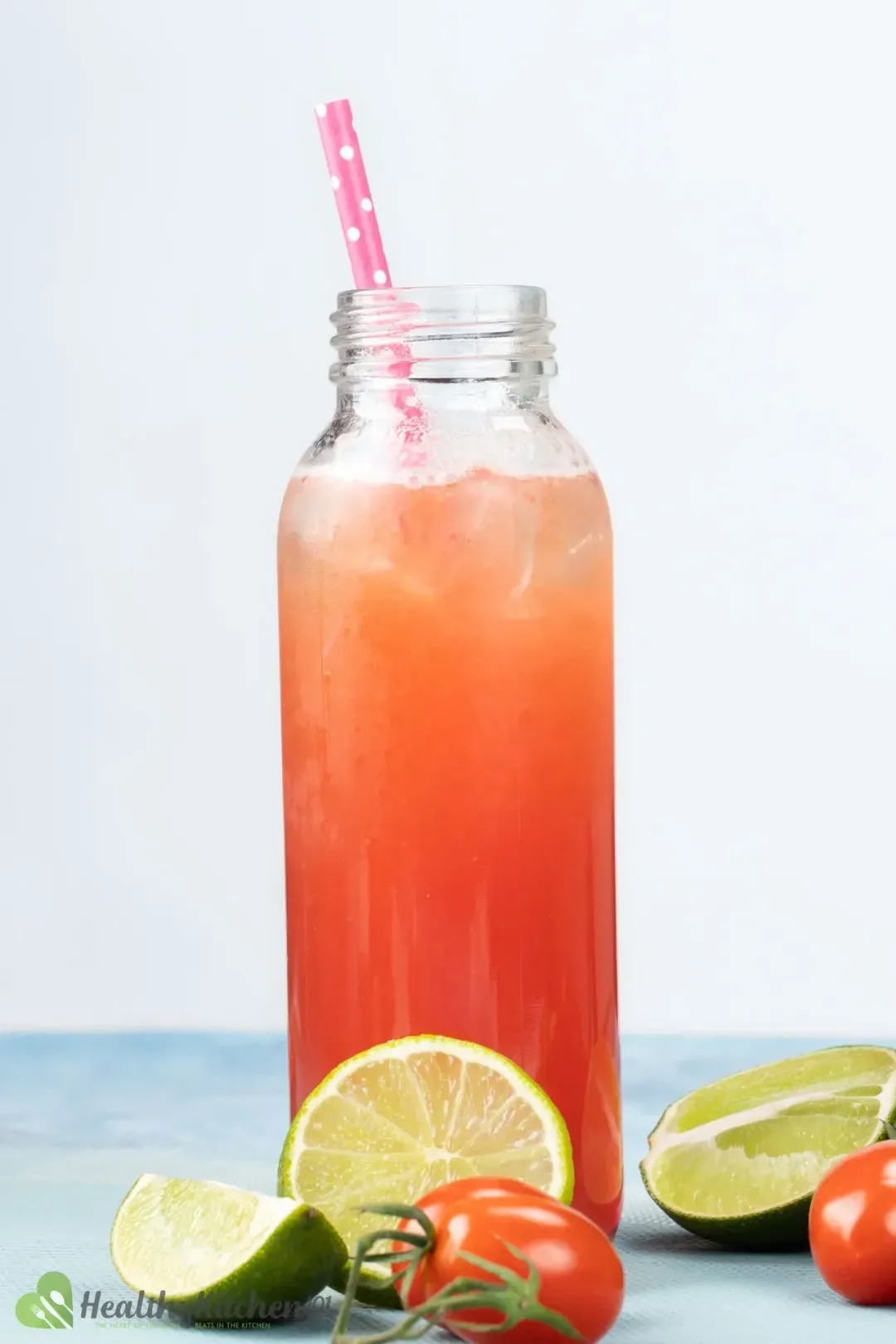 A narrow-neck bottle of tomato beer cocktail with a pink straw dunked in and fruits beneath it