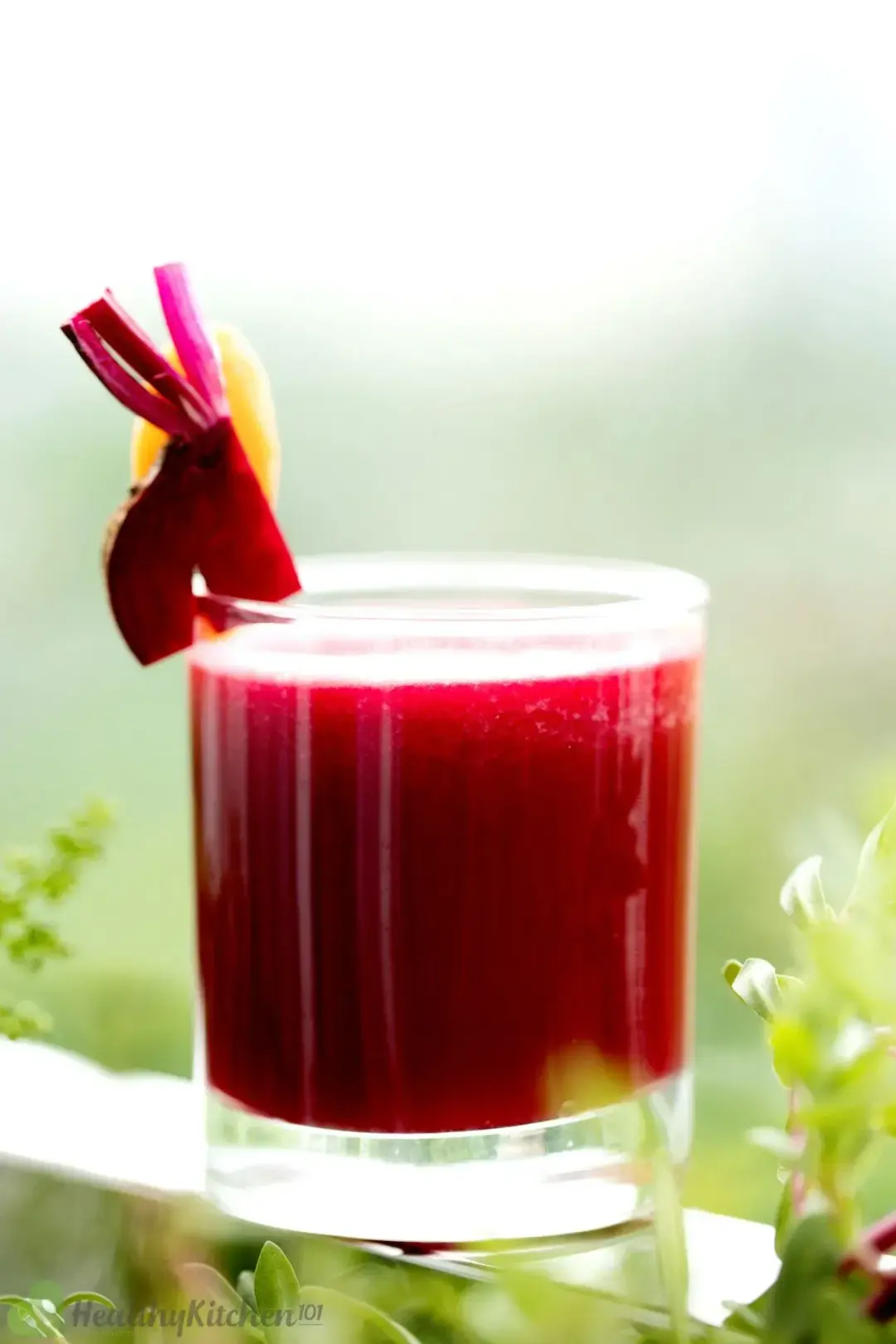 A short glass of red apple beet juice with a piece of beetroot on the rim, out in the open