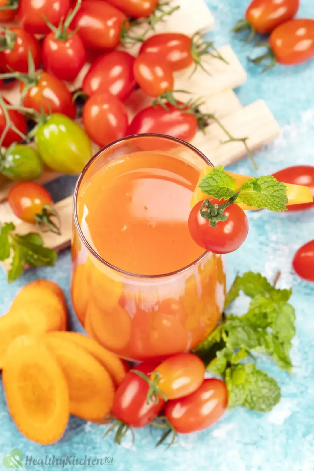 A shot from the top of a carrot tomato juice surrounded by mints, lots of cherry tomatoes, and carrot slices