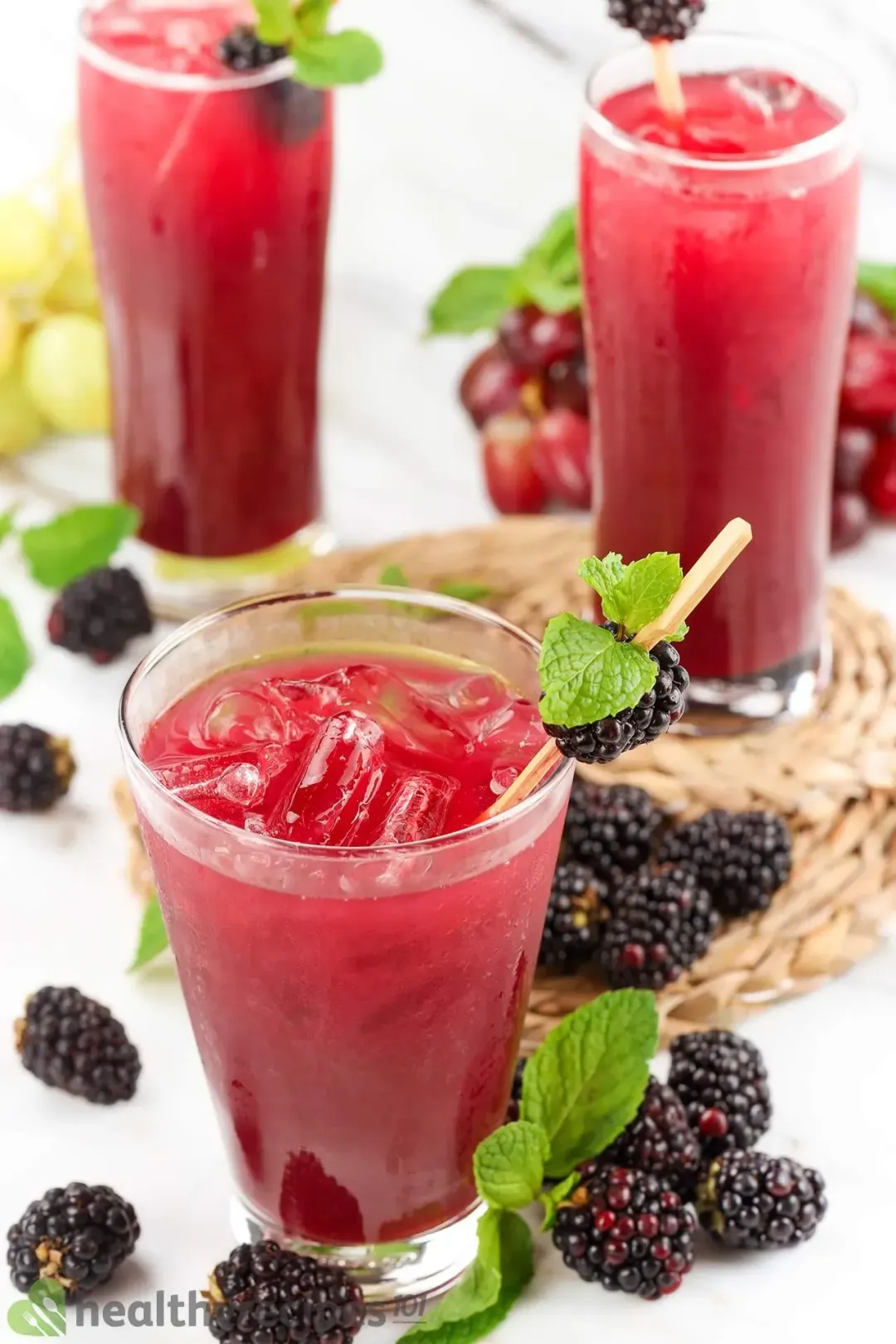 Three iced glasses of black berry juice drinks, with blackberries and mints all lying around