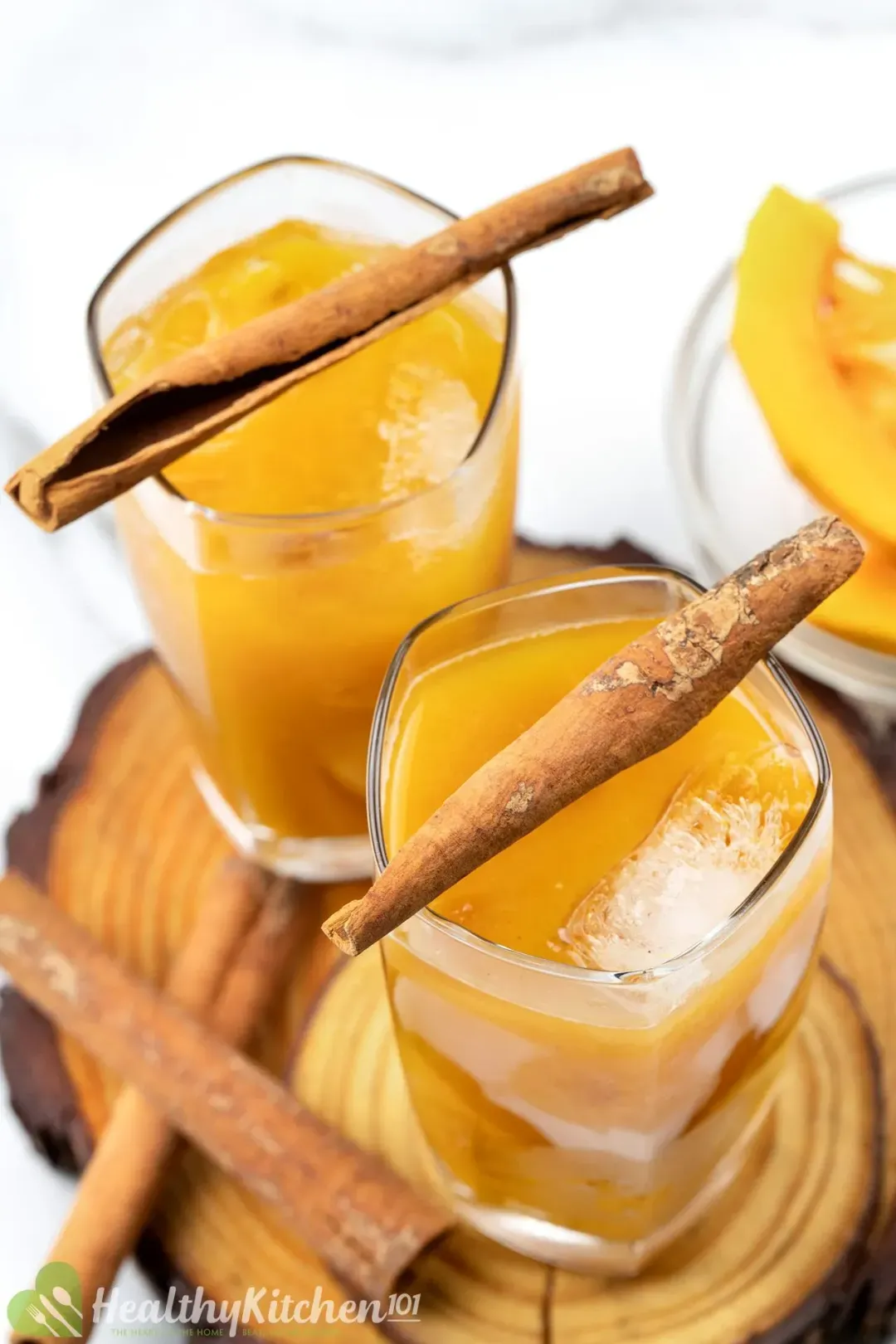 A close-up shot of two glasses of iced pumpkin juice adorned with cinnamon sticks on top of wooden coasters