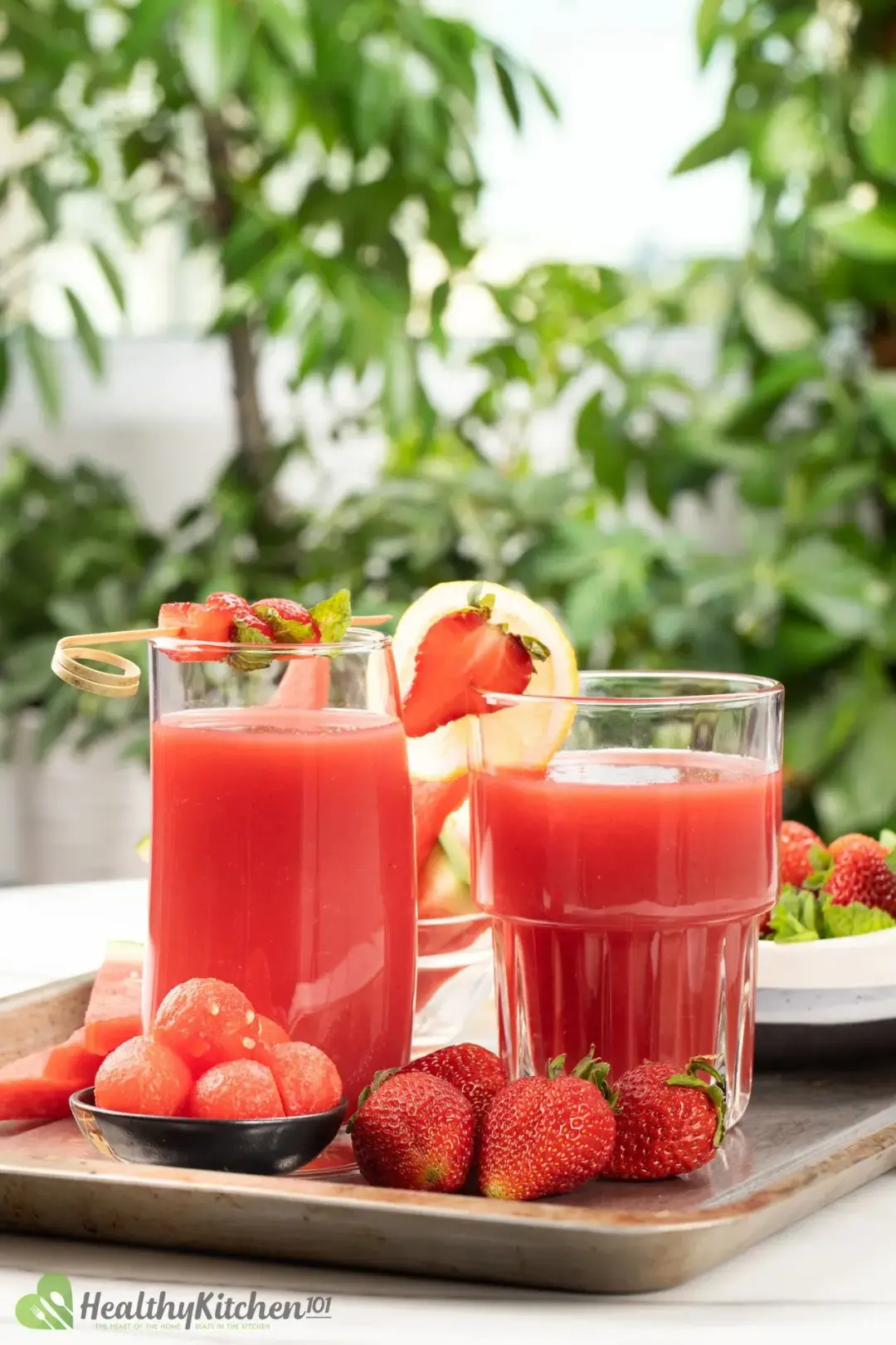 Two glasses of red juice in a steel tray with strawberries, lemon, and watermelon as decorations