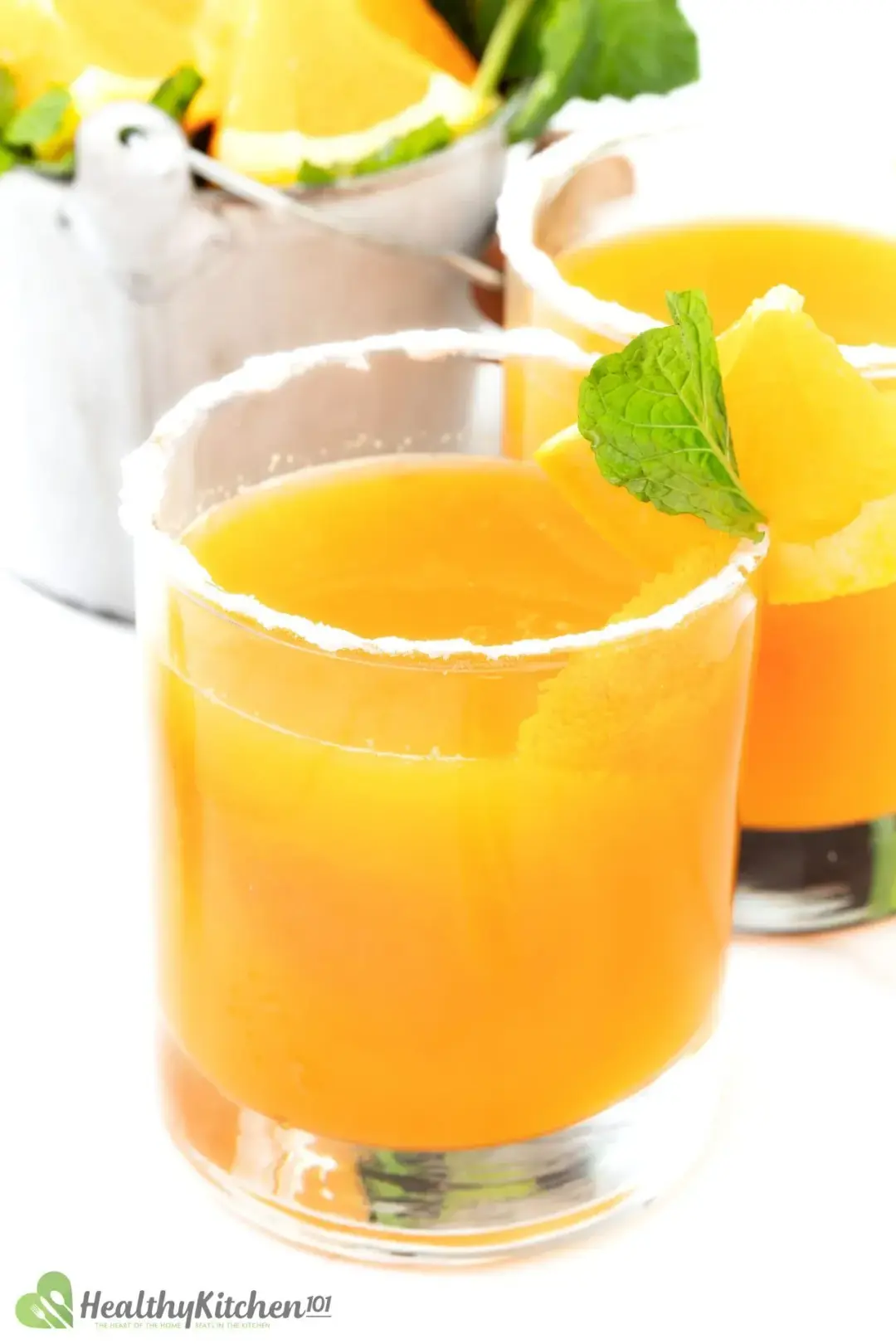 Two glasses of orange juice cocktail placed side by side, with powdered sugar on the rim and mint sprigs