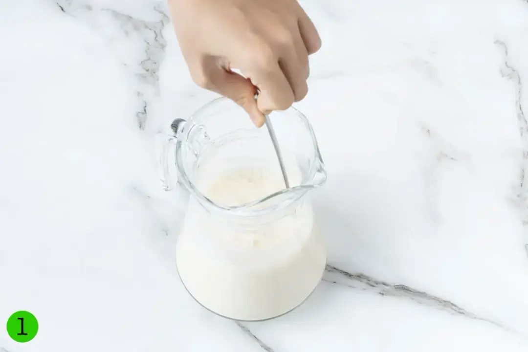 A spoon stirring a pitcher of milk