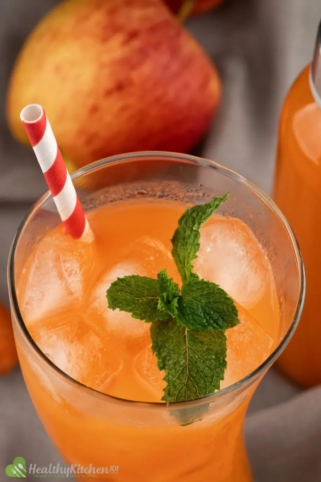 A close up shot of an iced carrot drink garnished with mints and with a red striped straw dunked in