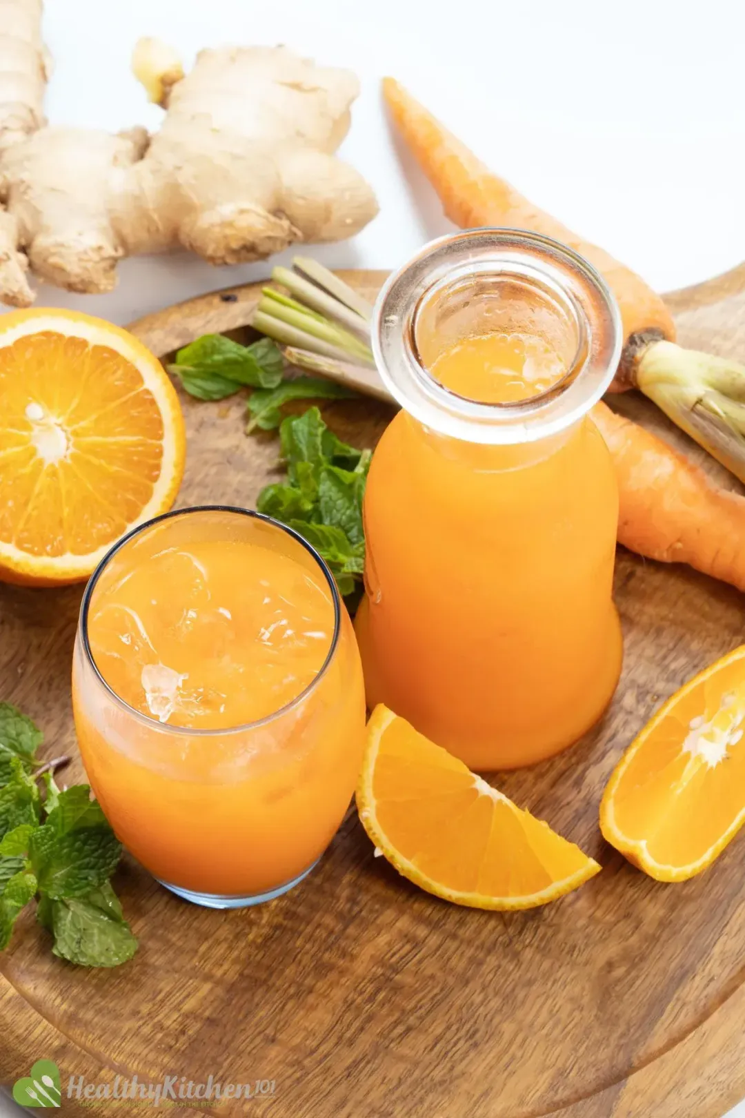 An iced glass and a jar of carrot orange juice, put on a wooden cutting board with mints and orange wedges