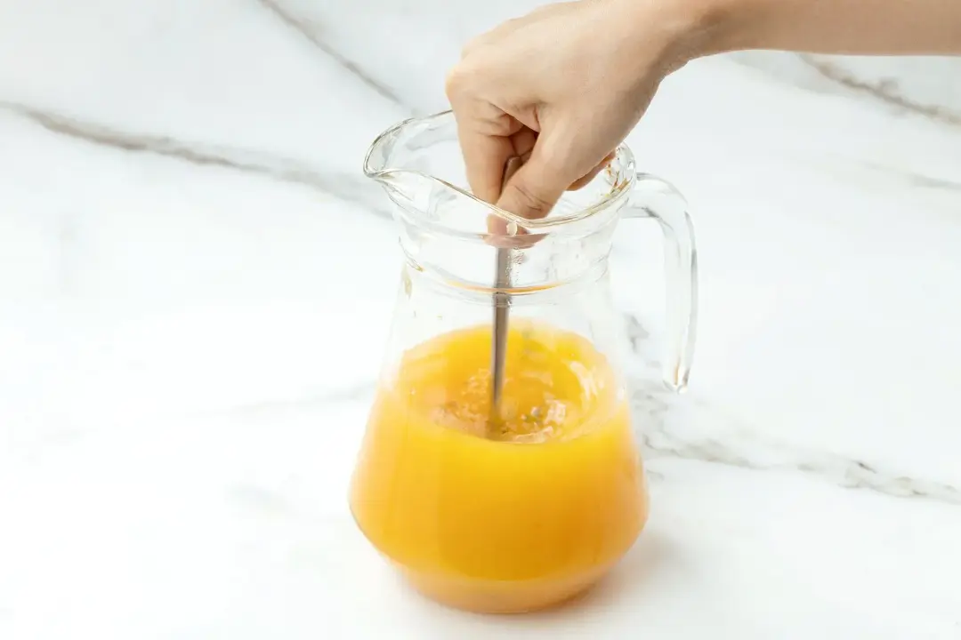 Stirring an orange liquid inside a clear pitcher