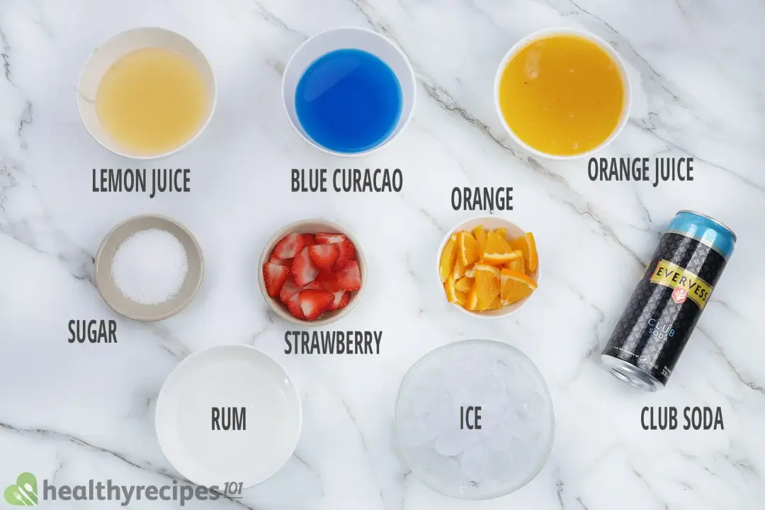 Ingredients for green jungle juice, including bowls of blue curacao, orange juice, lemon juice, orange slices, strawberry slices, ice, soda, rum, and sugar
