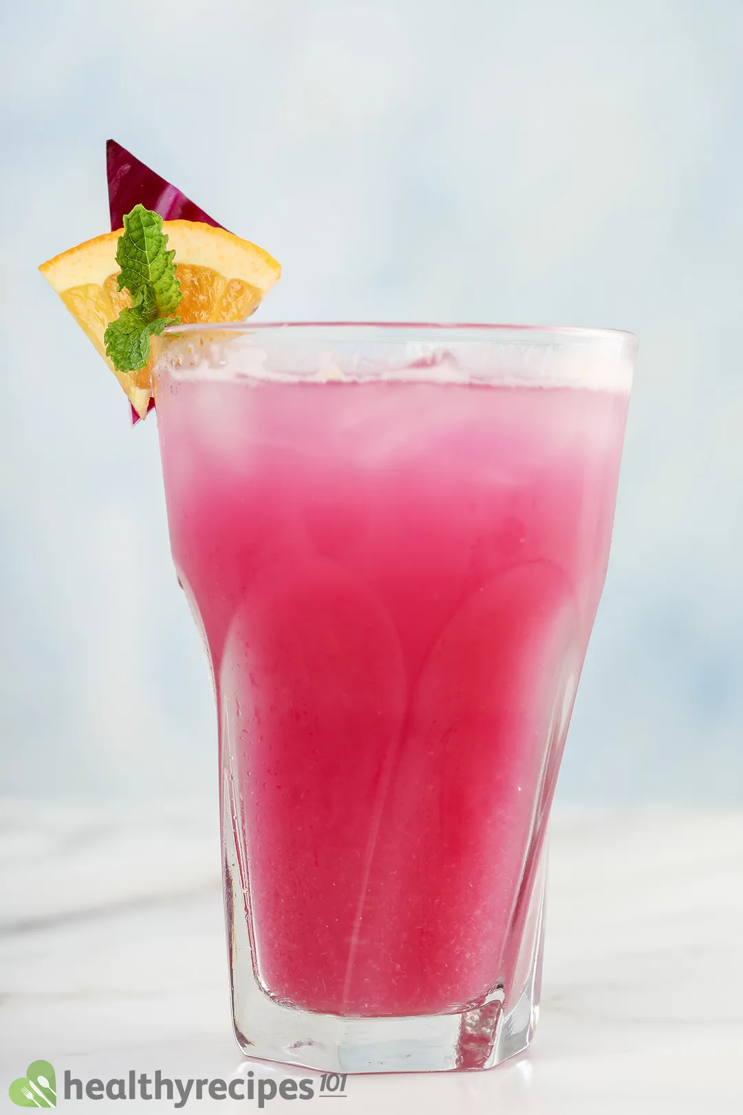 a glass of red cabbage juice decorated with orange slice, mint leaf