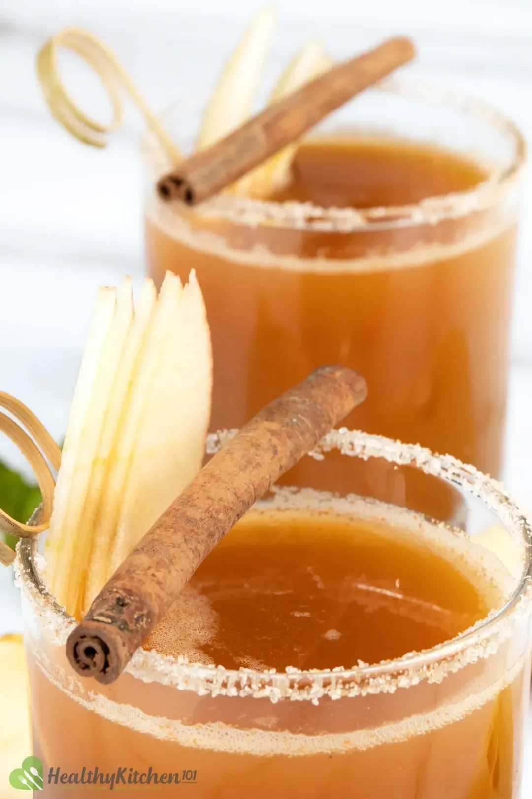 Two glasses of apple juice and vodka cocktail, topped with a cinnamon stick and apple slices